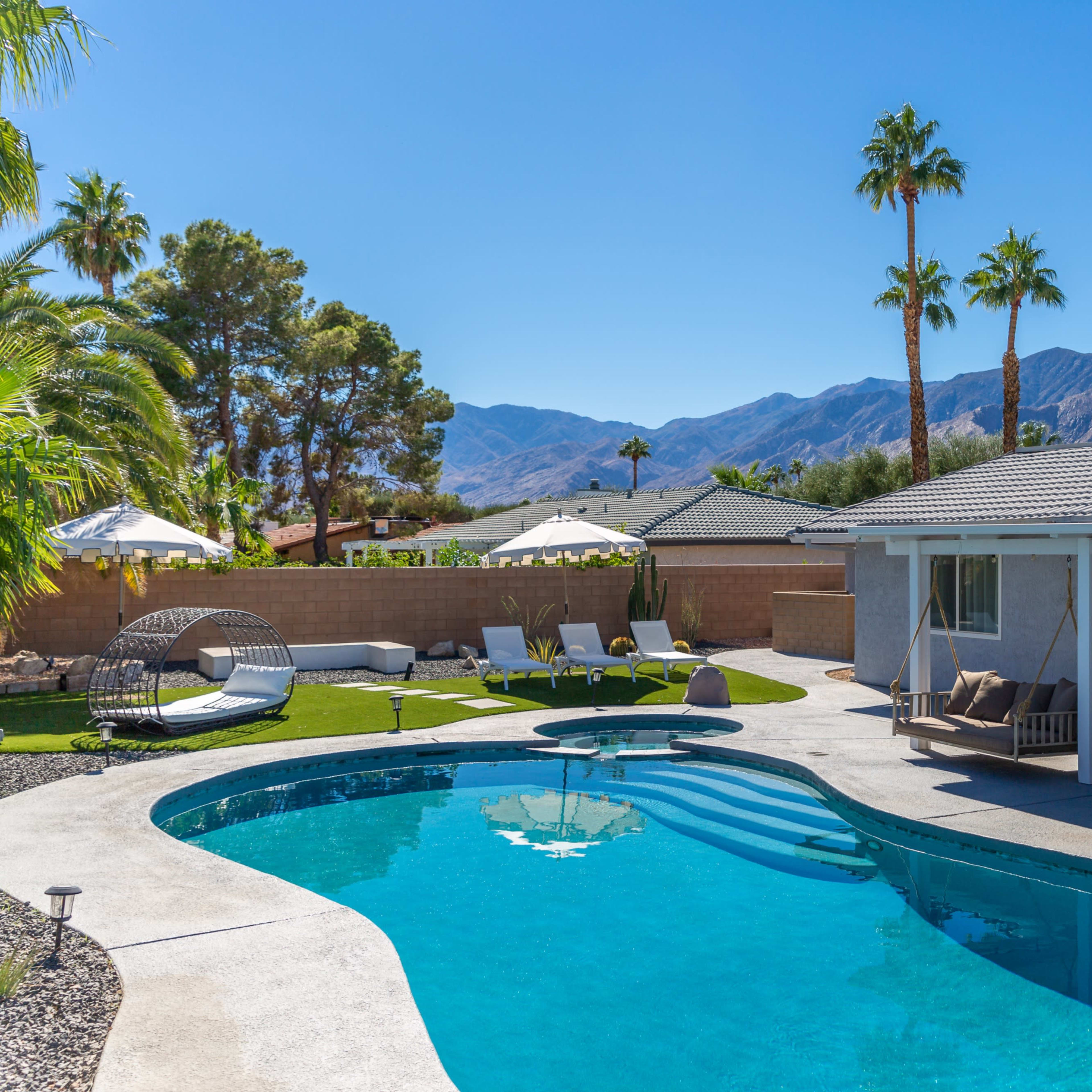 A backyard pool area surrounded by palm trees, lounge chairs, and a view of mountains in the background.
