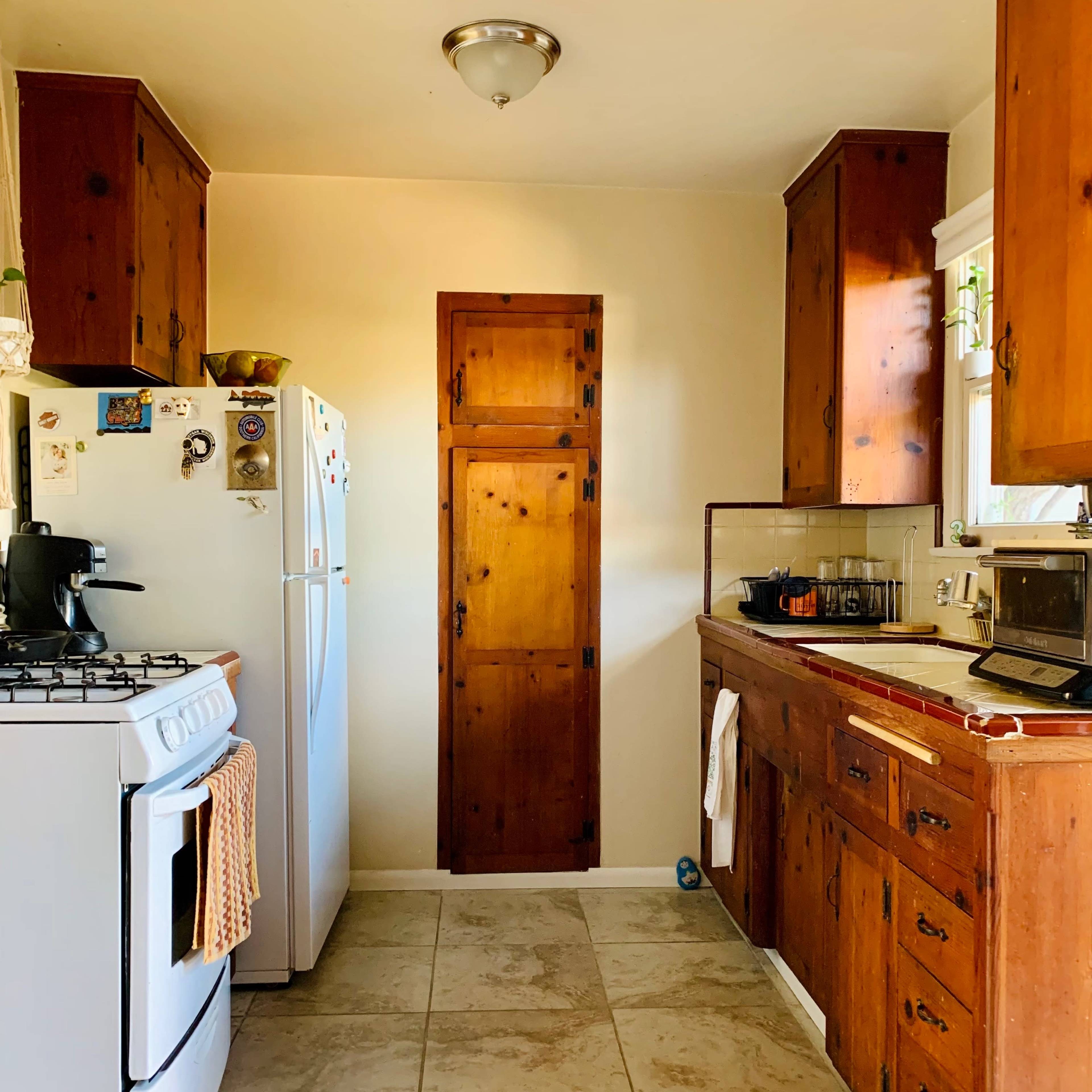 A kitchen with wooden cabinets, a white refrigerator, a gas stove, and a door leading to another room.