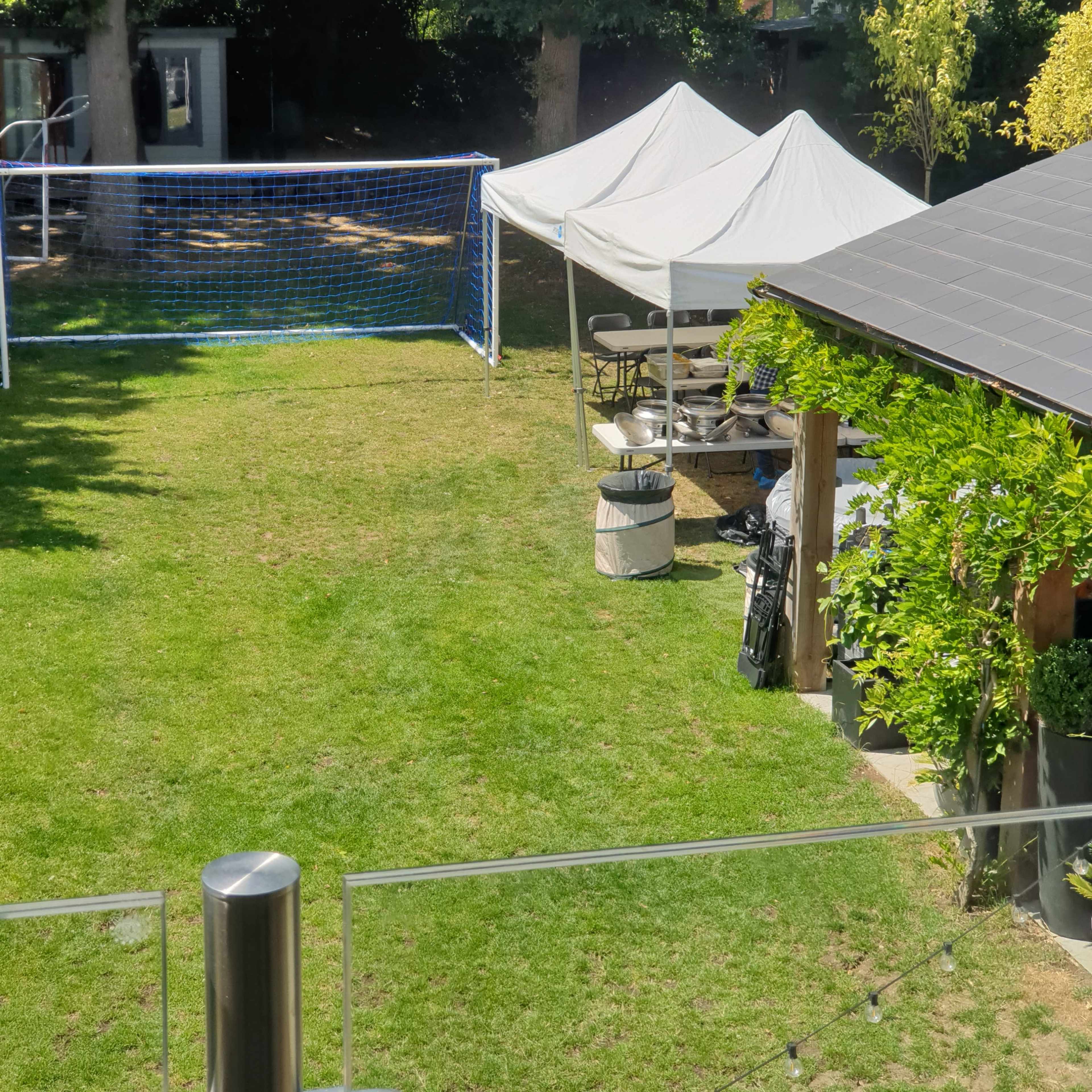 A backyard with a soccer goal, a tent, and a seating area surrounded by trees.