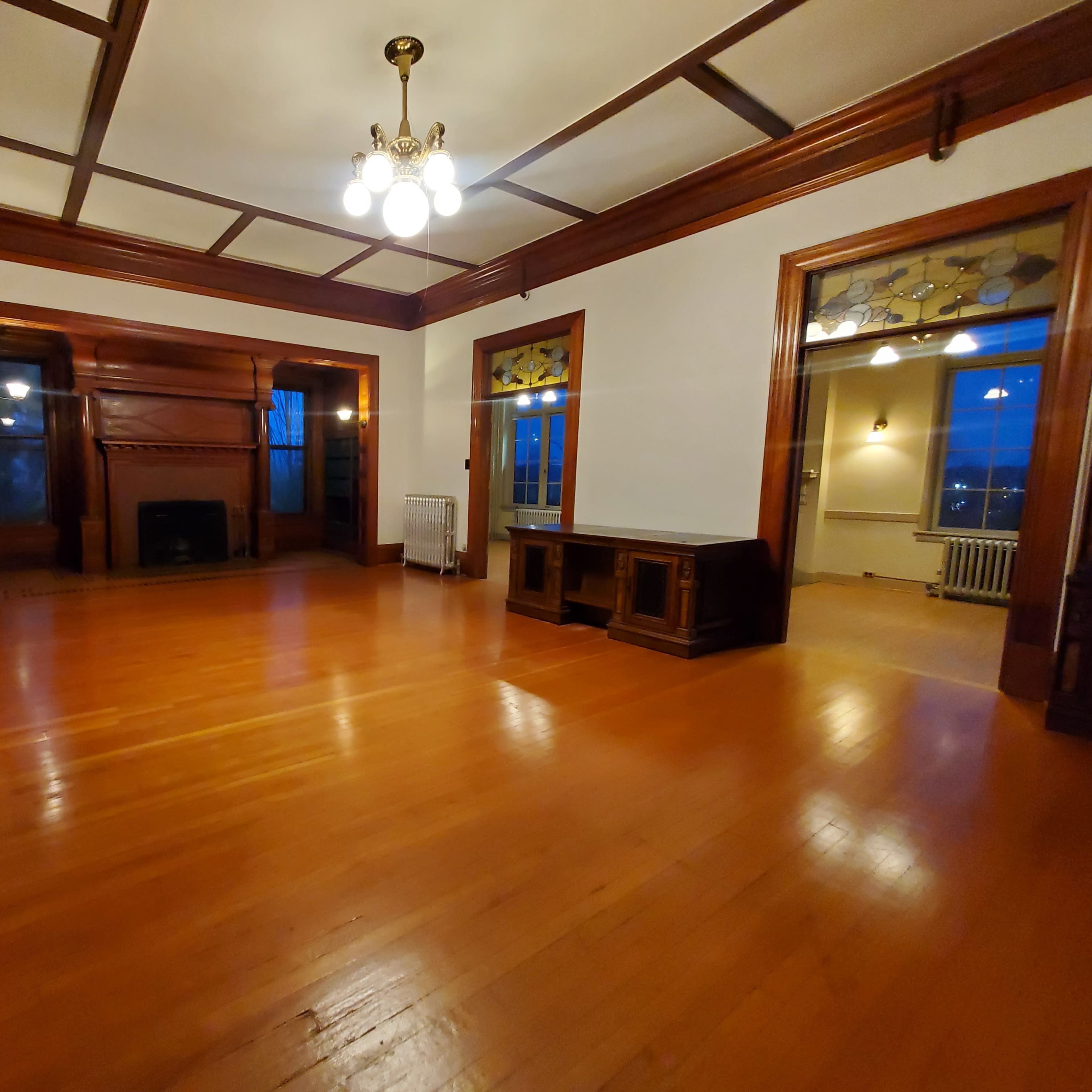 A spacious, empty room with wooden floors, a fireplace, and large windows.