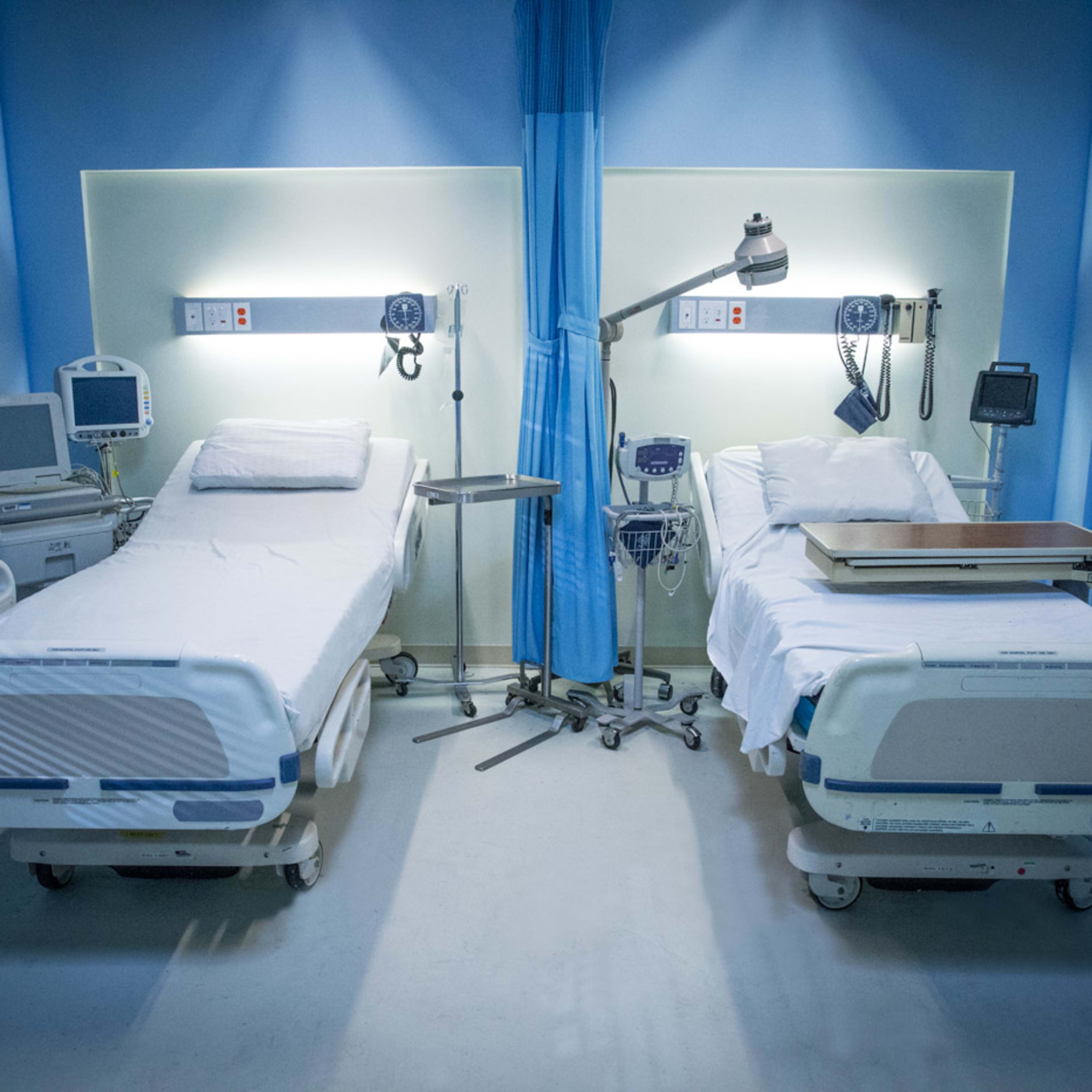 A hospital room with two unoccupied beds, medical equipment, and a blue and white color scheme.