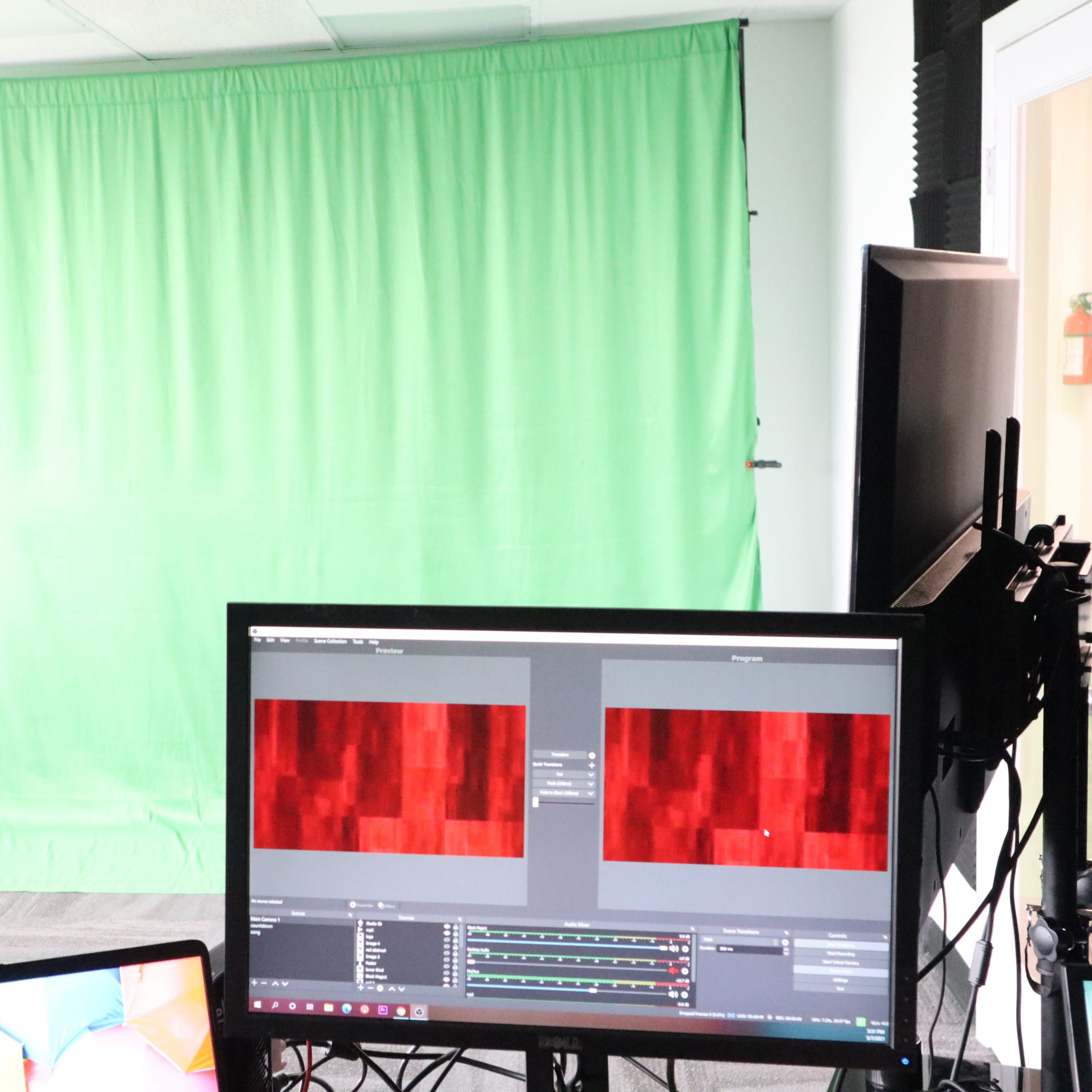A studio setup with a green screen backdrop and two computer monitors displaying abstract patterns.