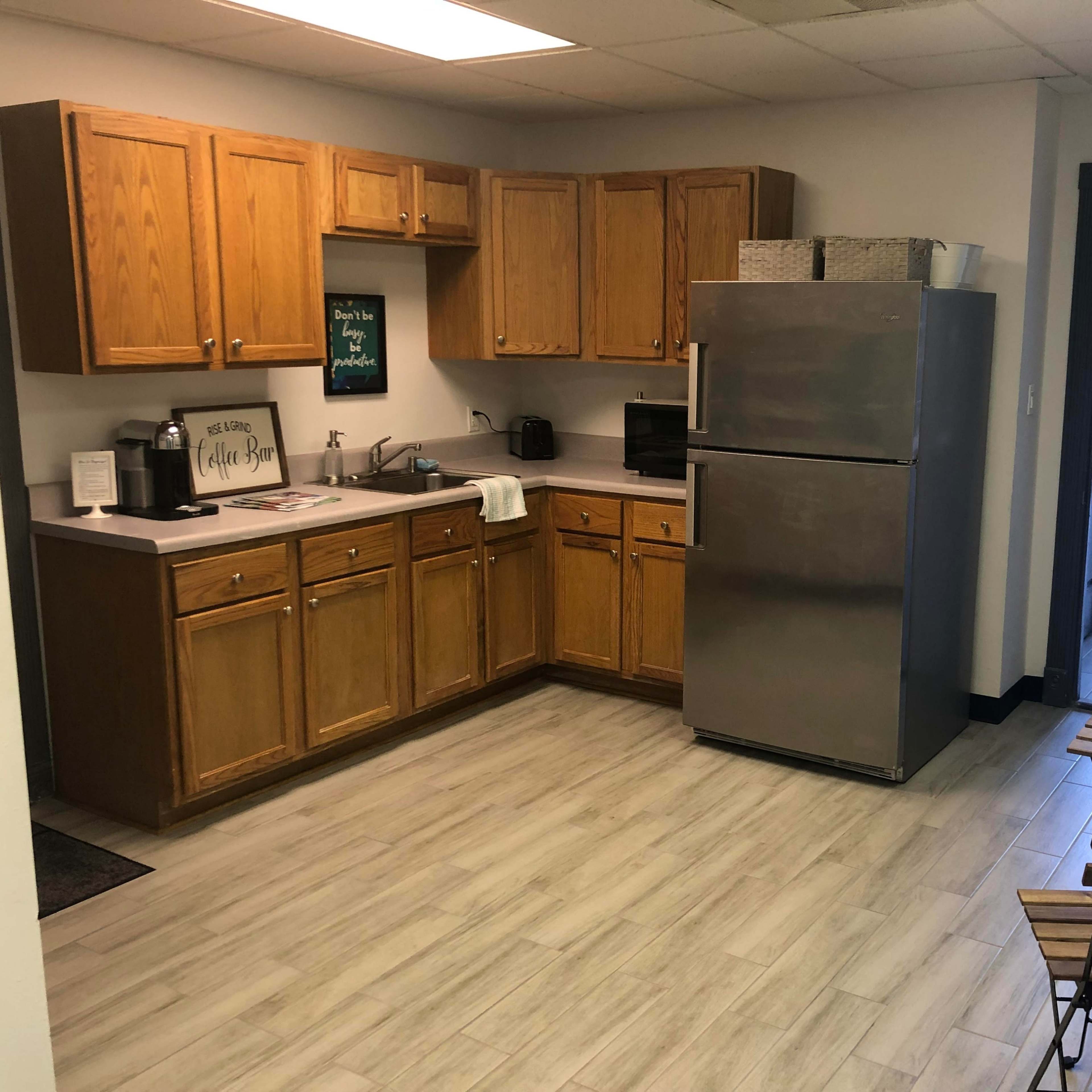 A kitchen with wooden cabinets, a stainless steel refrigerator, a small table with chairs, and a doorway leading outside.