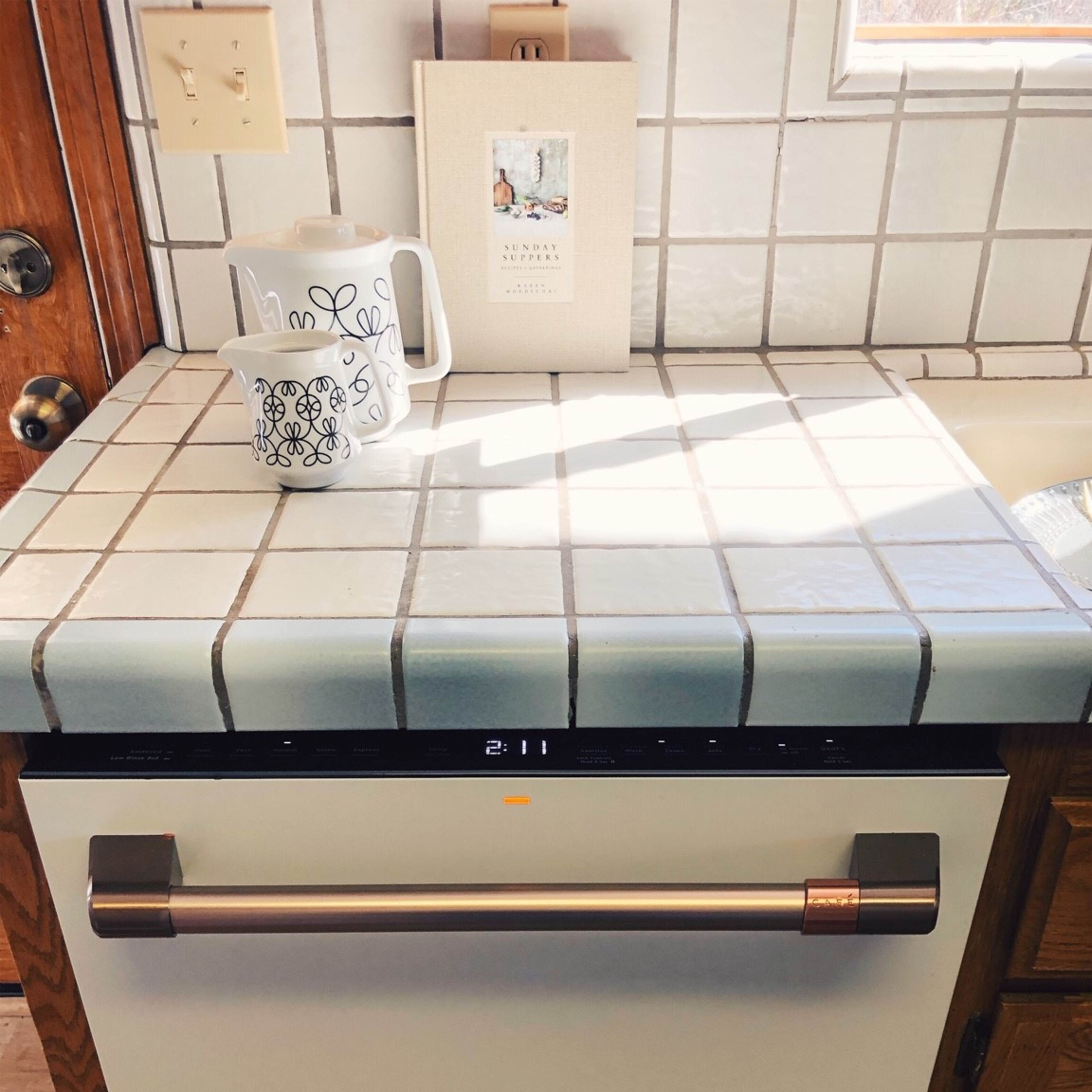 A kitchen countertop with a white dishwasher, a decorative mug, and a small notebook beside it.