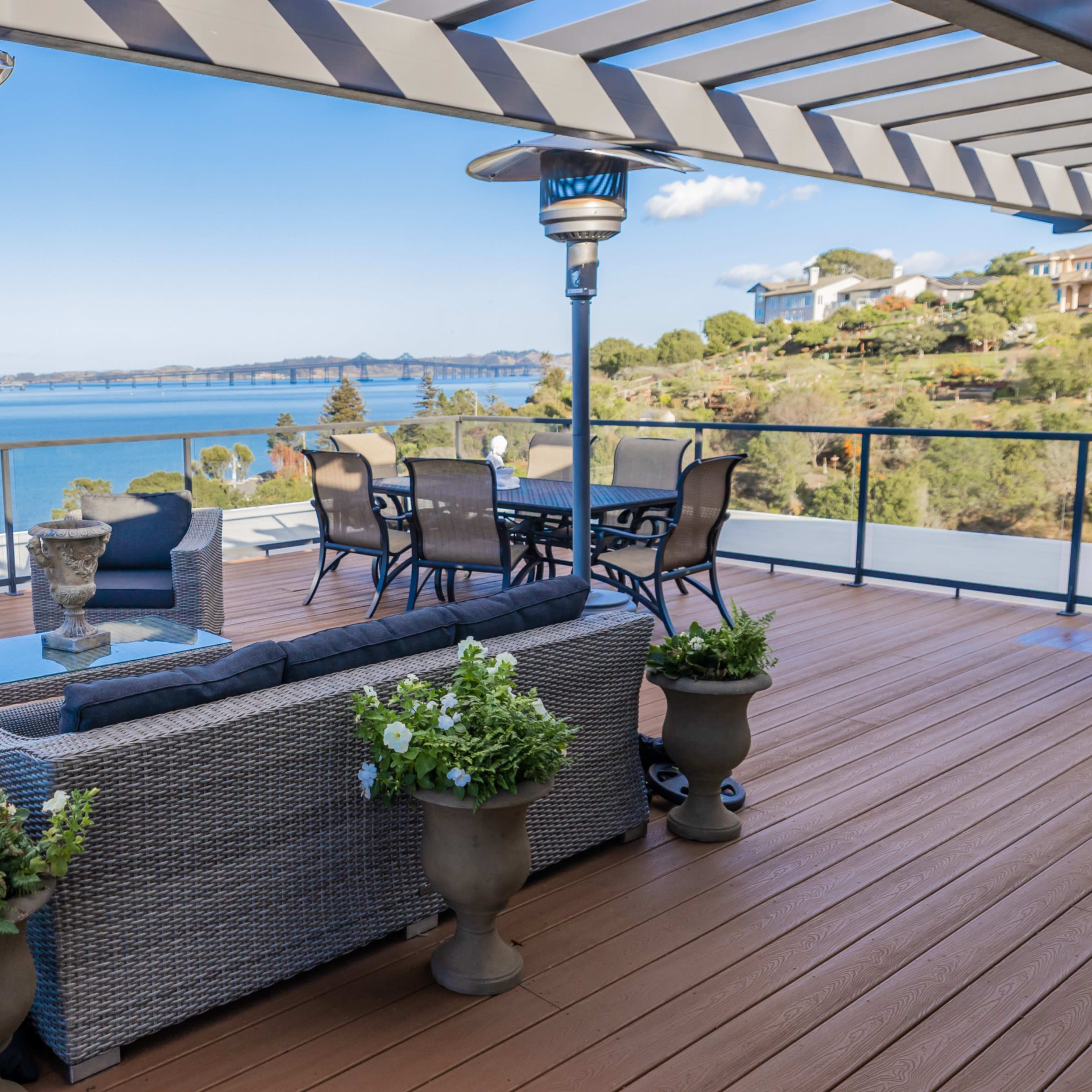 A spacious deck with outdoor furniture overlooking a body of water and a distant bridge.