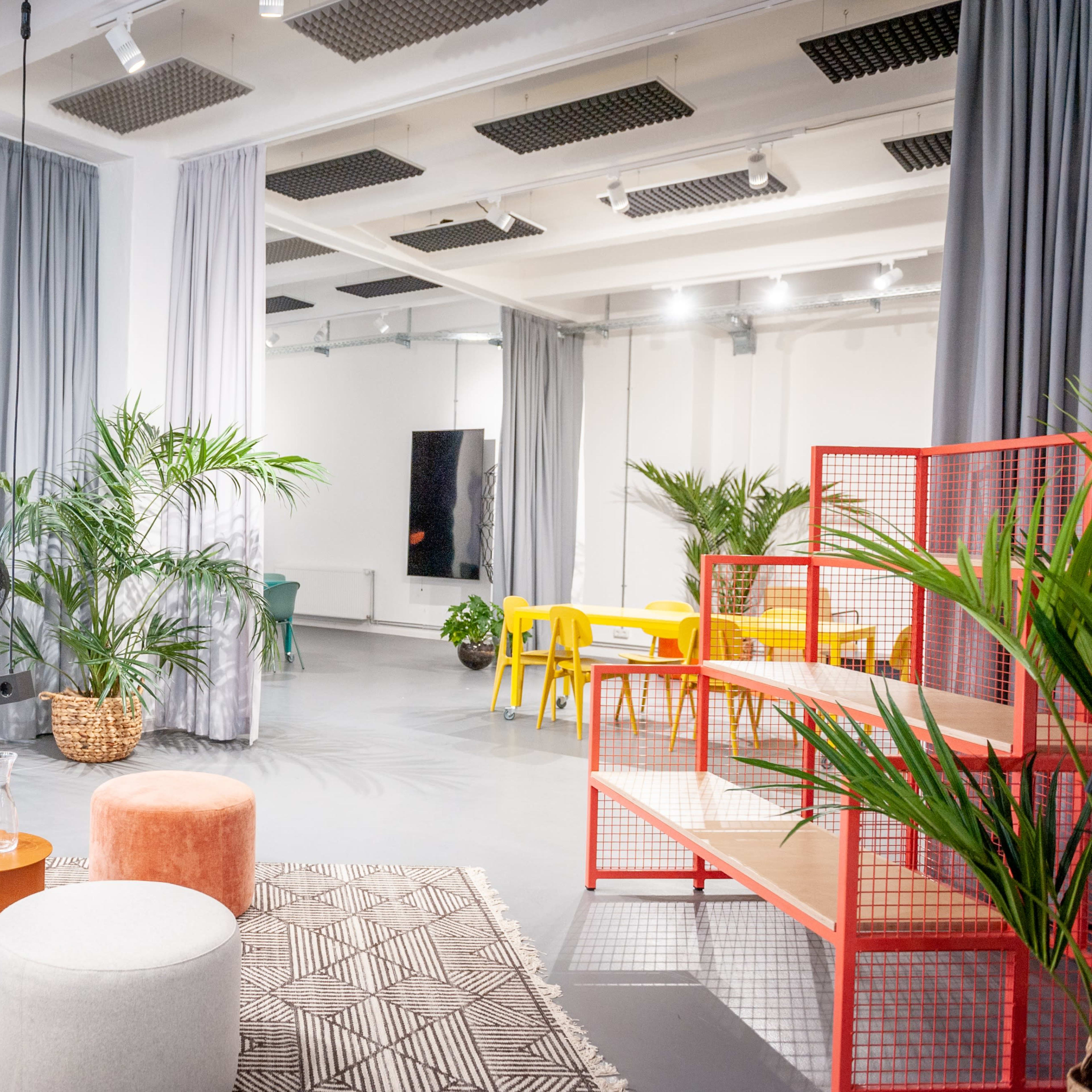 A modern, open space with various seating options, a bar area, and indoor plants arranged around a light-colored floor.
