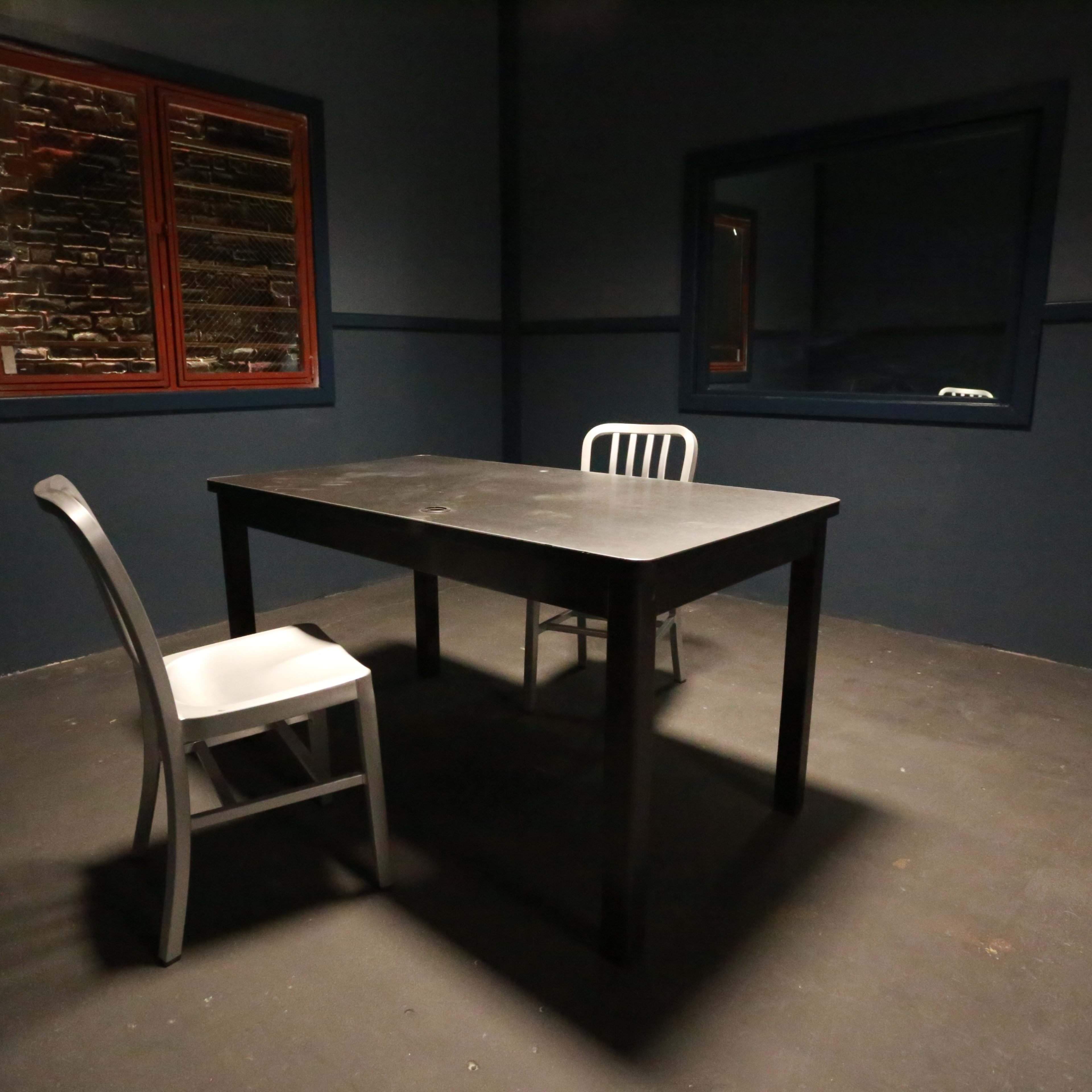 A dimly lit room with a black table, two chairs, and dark blue walls, featuring a window with red frames.