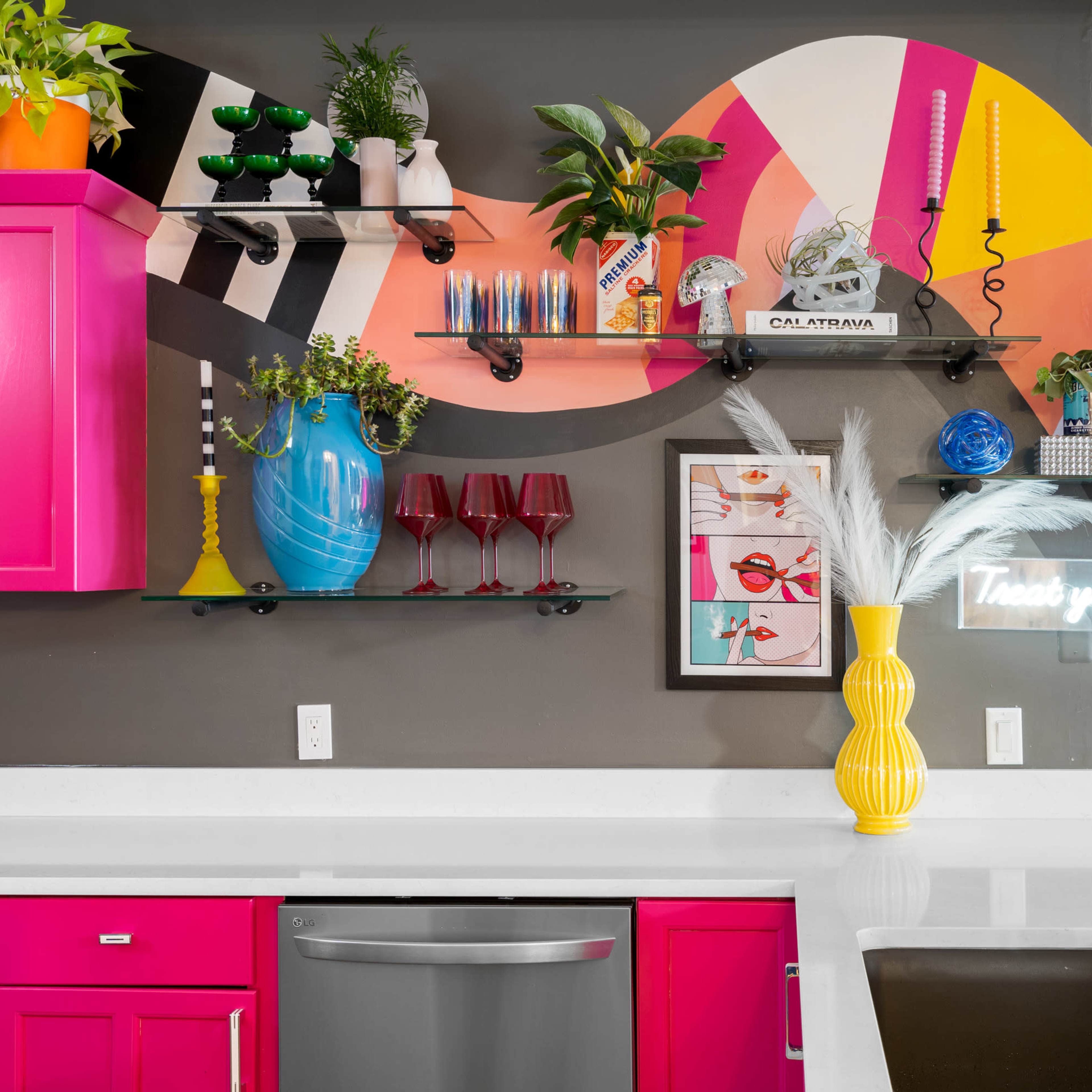 A vibrant kitchen featuring bright pink cabinets, a variety of colorful decorative items on open shelves, and a modern sink with a sleek faucet.