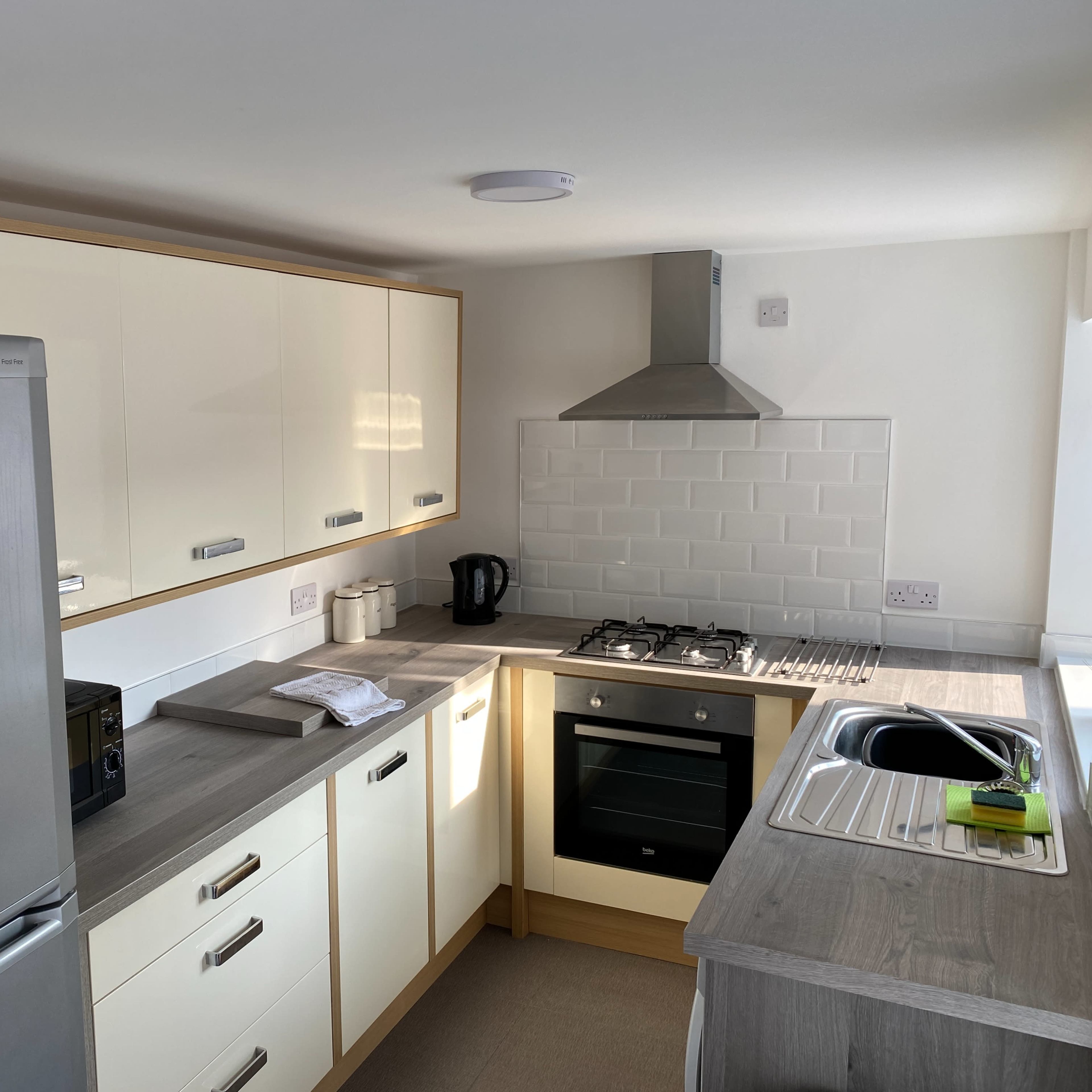 A modern kitchen with a silver refrigerator, a gas stove, an oven, and a sink, featuring light-colored cabinetry and a tiled backsplash.