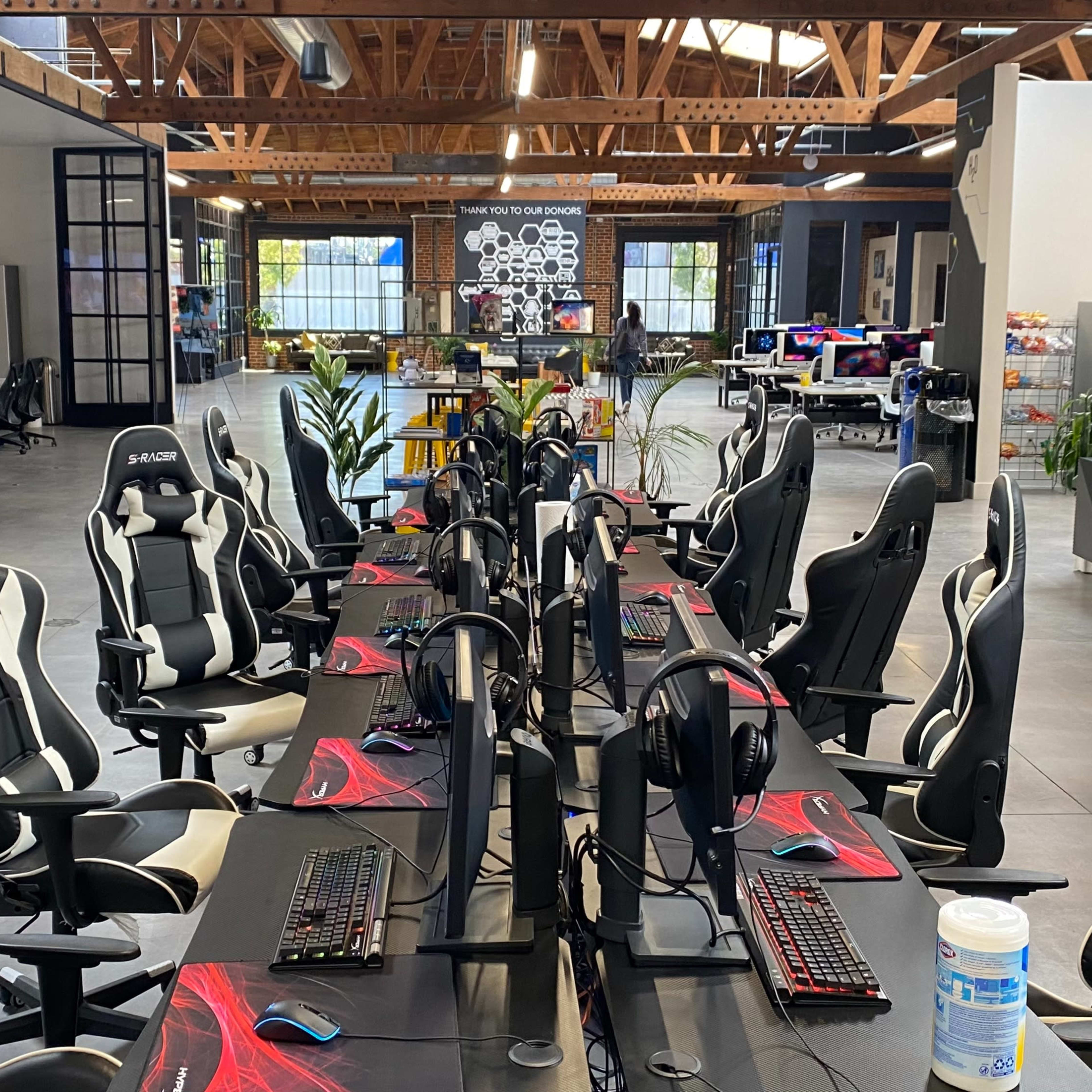 A modern open office space with several gaming desks equipped with monitors and gaming chairs arranged in a row.