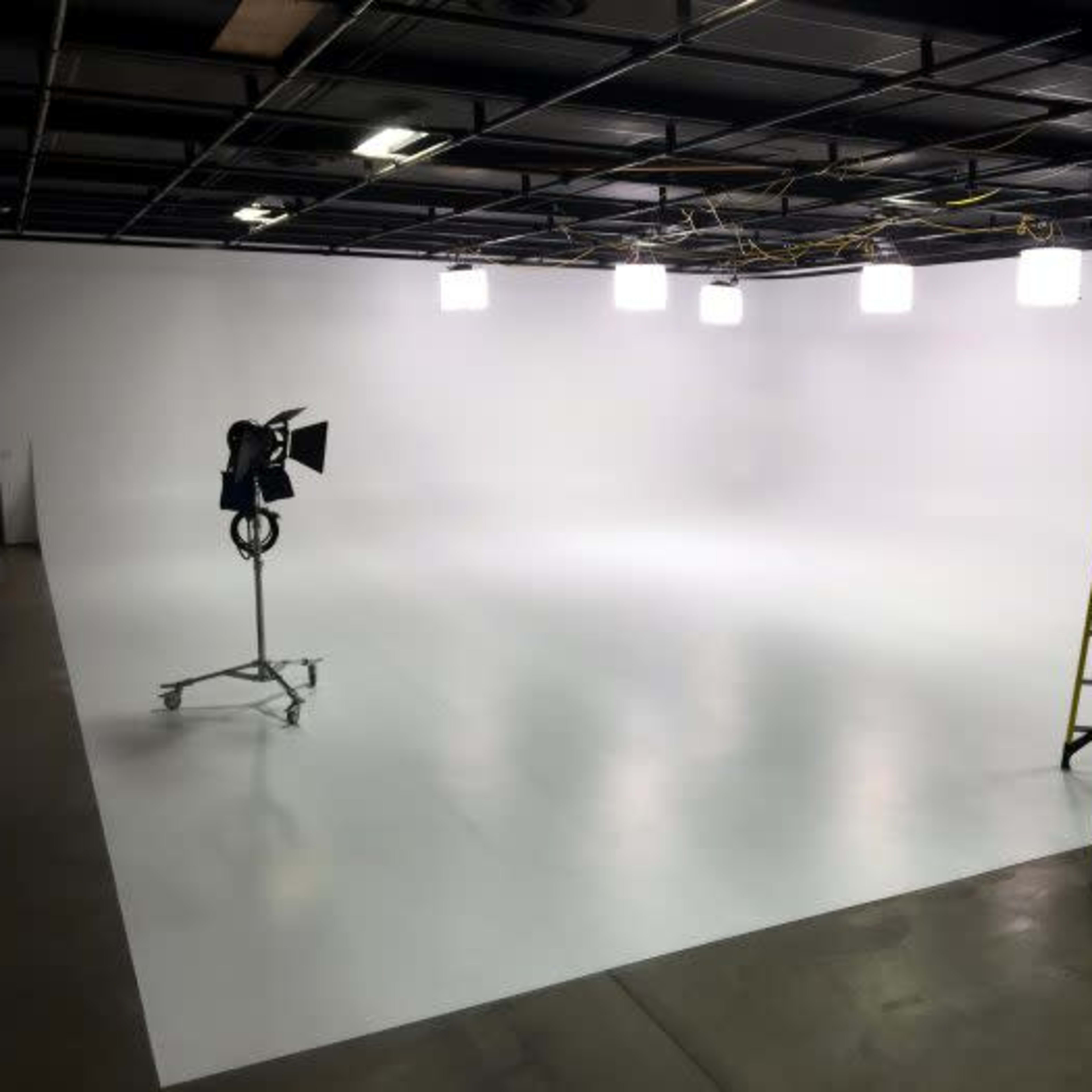 A sparse photography studio with a white backdrop, a ladder, and studio lights on stands.