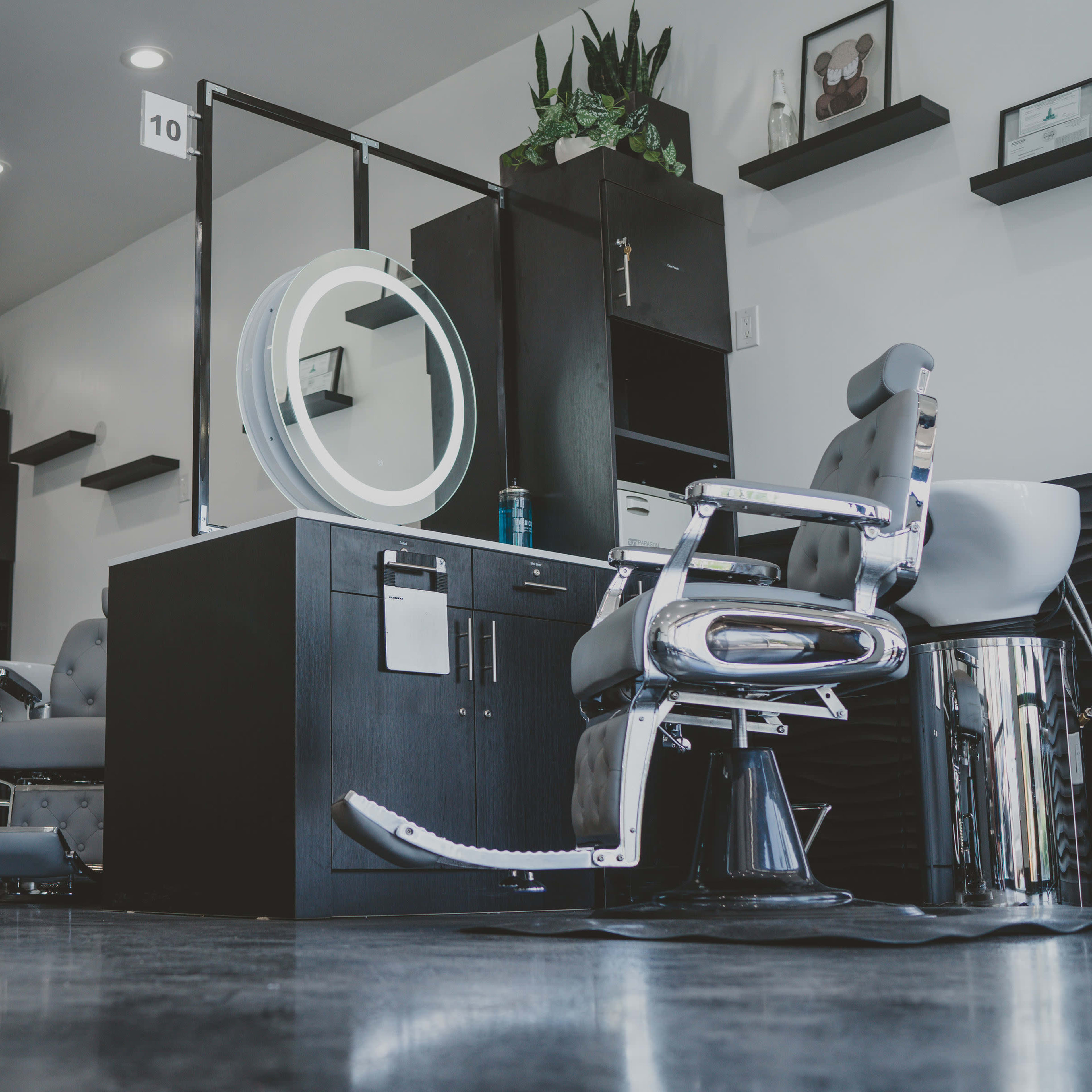 A modern hair salon interior with two styling stations featuring large round mirrors, black cabinetry, and sleek silver salon chairs.