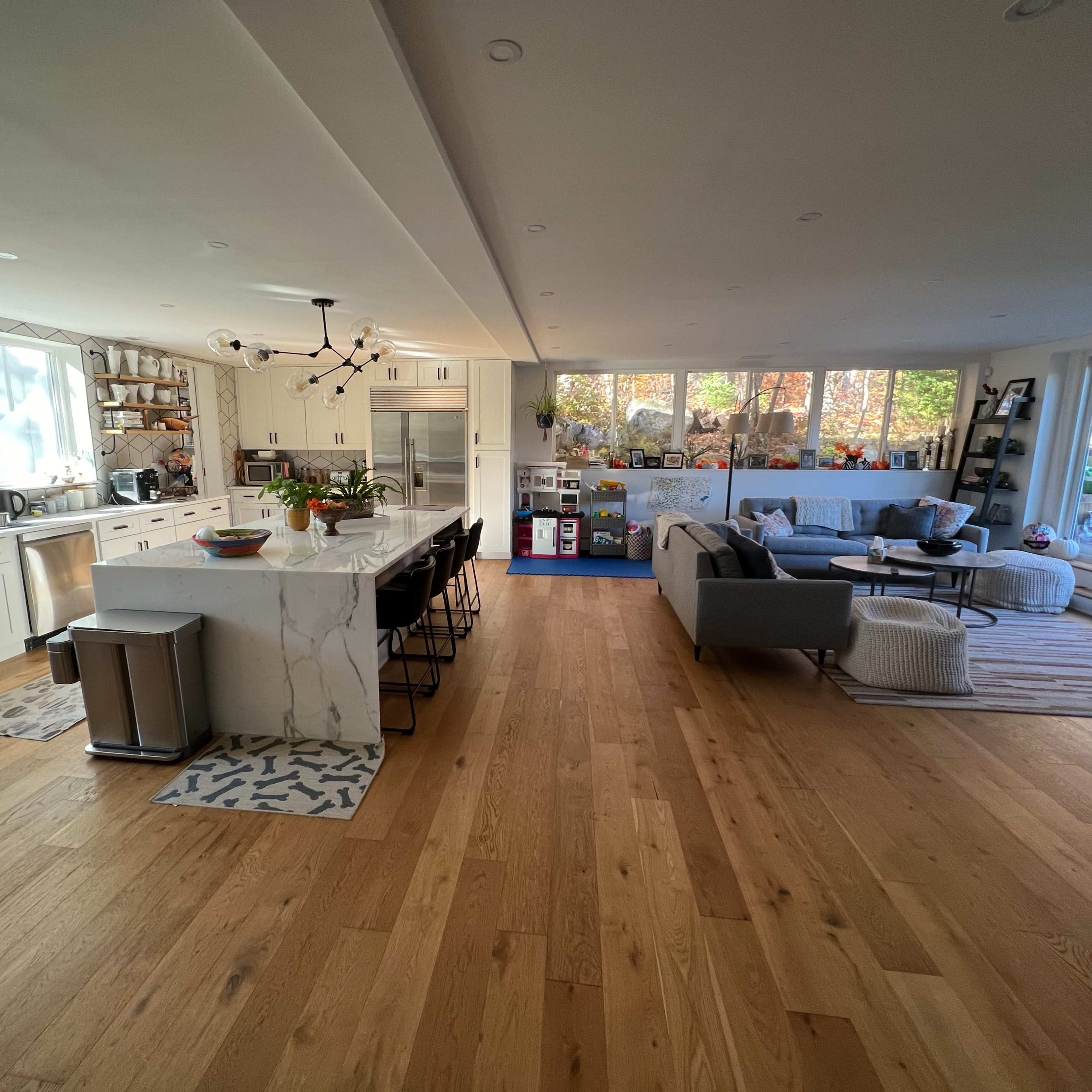 A spacious kitchen and living area feature a large island with bar seats, modern appliances, and large windows that allow natural light to fill the space.