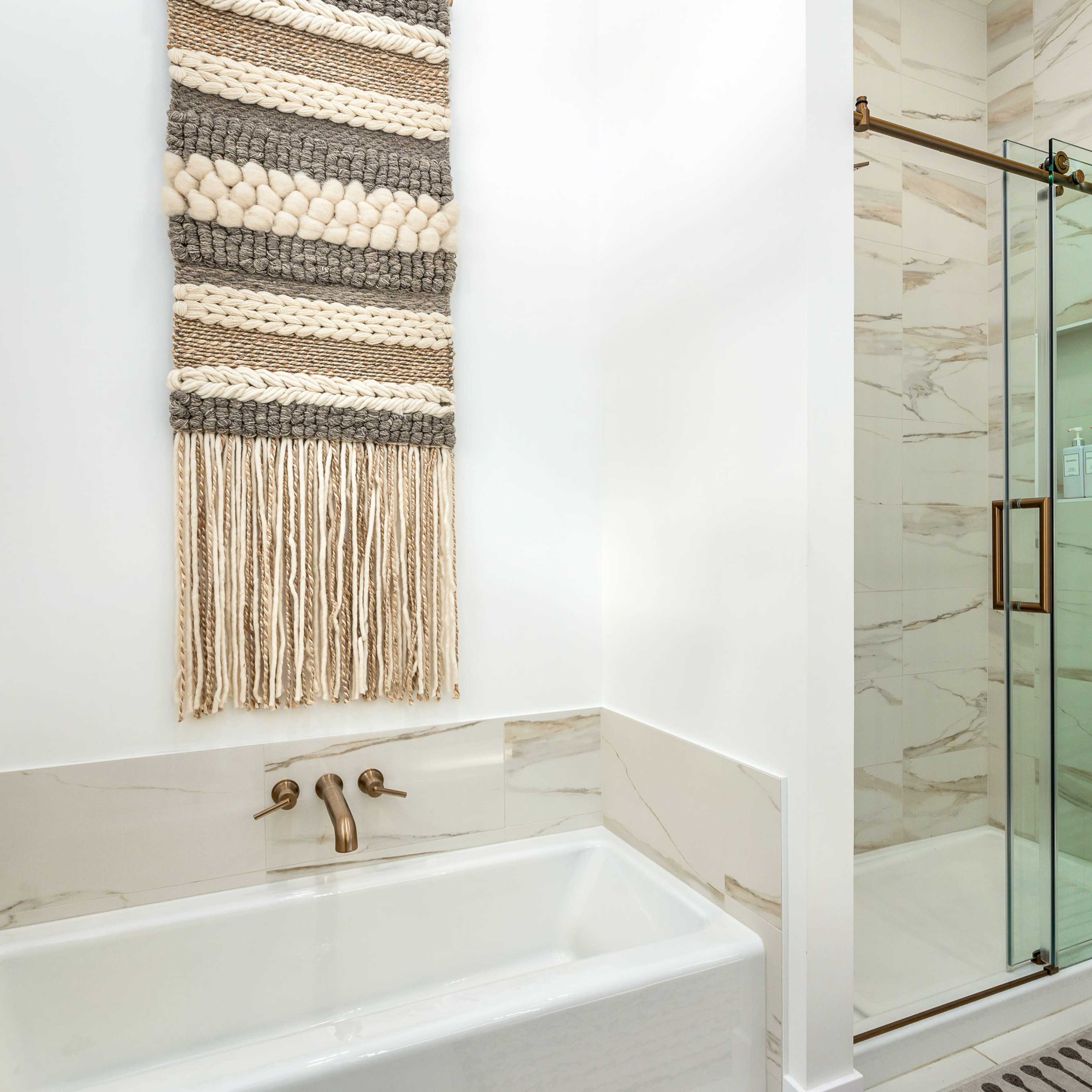 A modern bathroom featuring a freestanding bathtub, a glass shower enclosure, and a wall adorned with woven decor.