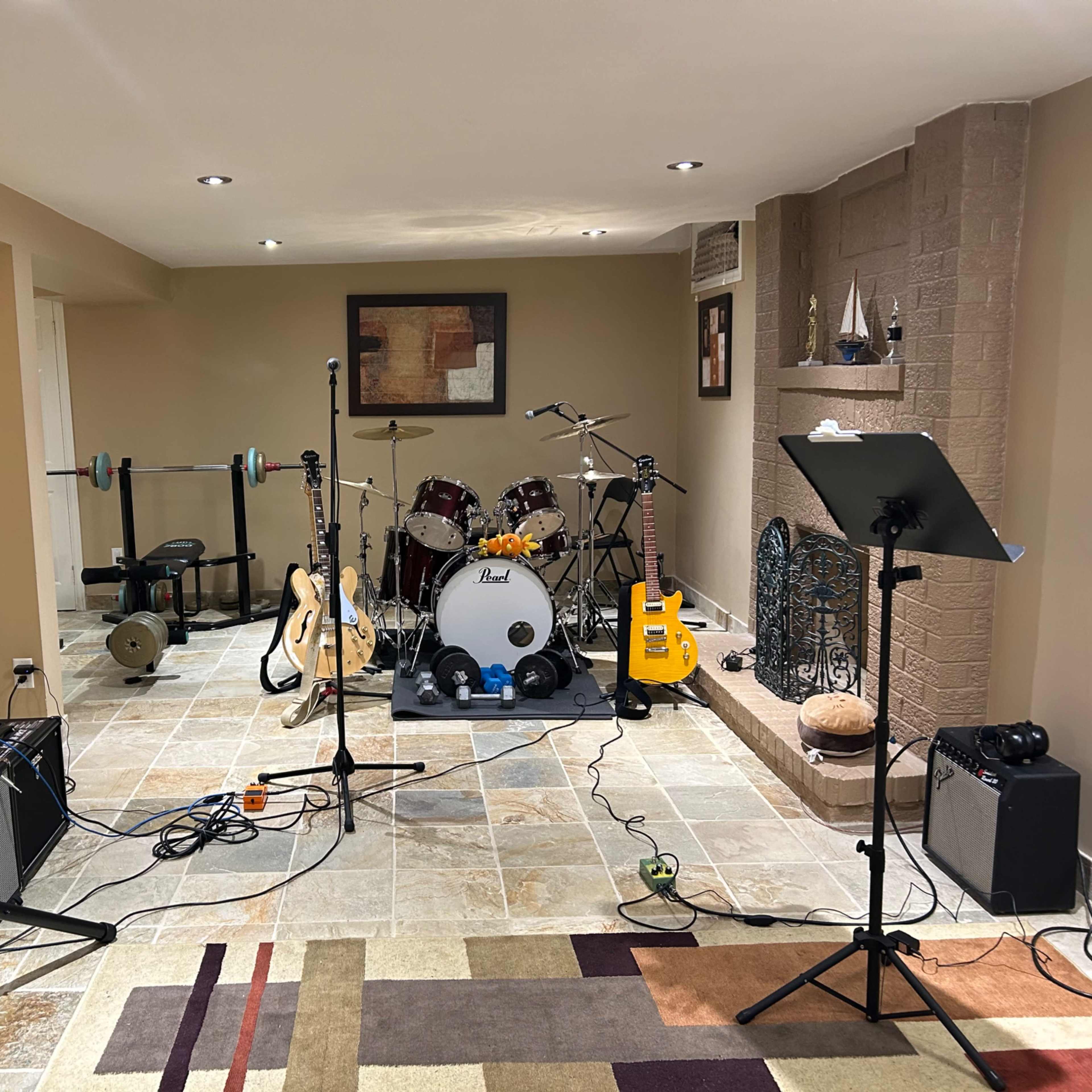 The room features a home music setup with a drum kit, various guitars, amplifiers, and exercise equipment.