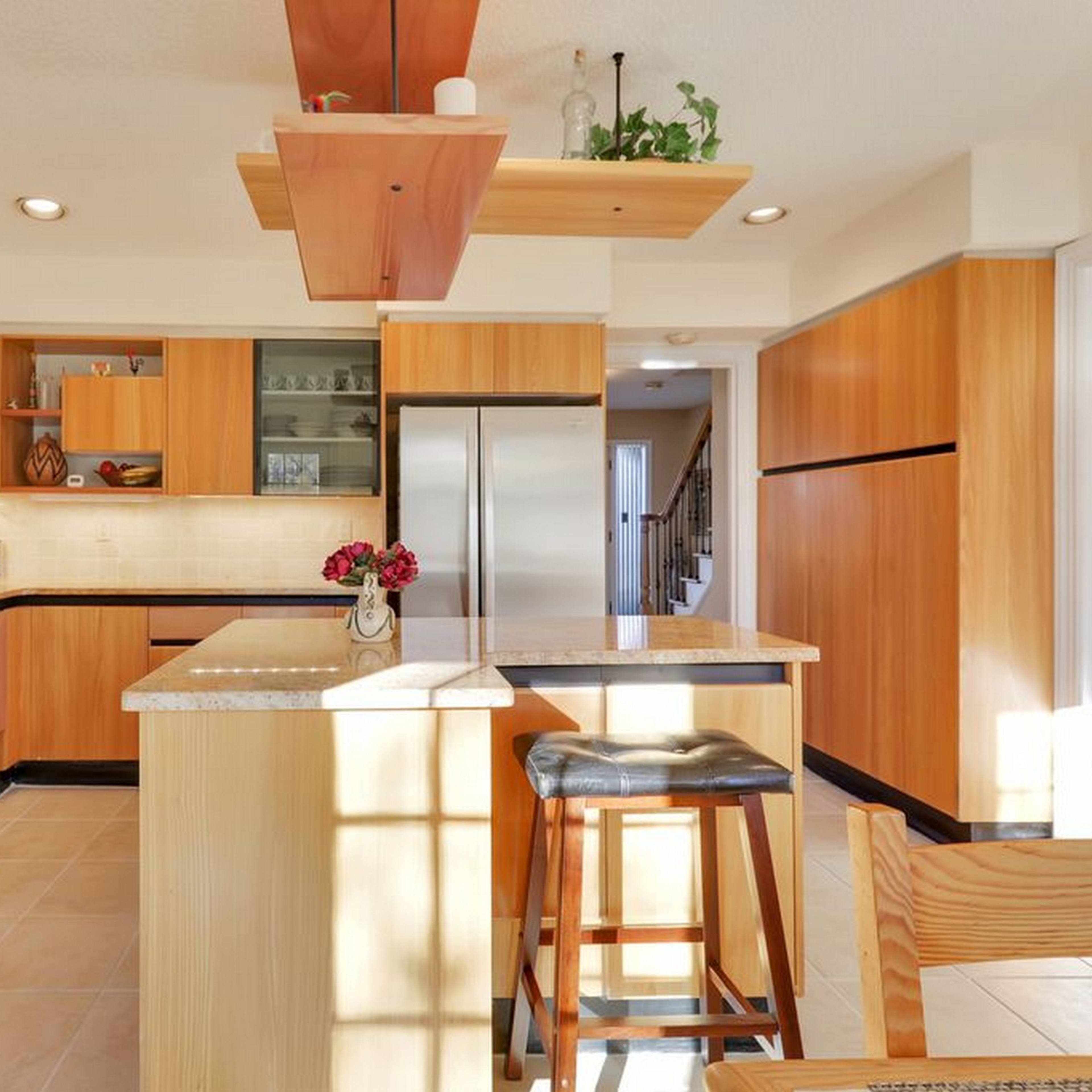 The kitchen features wooden cabinetry, a central island with seating, and stainless steel appliances.