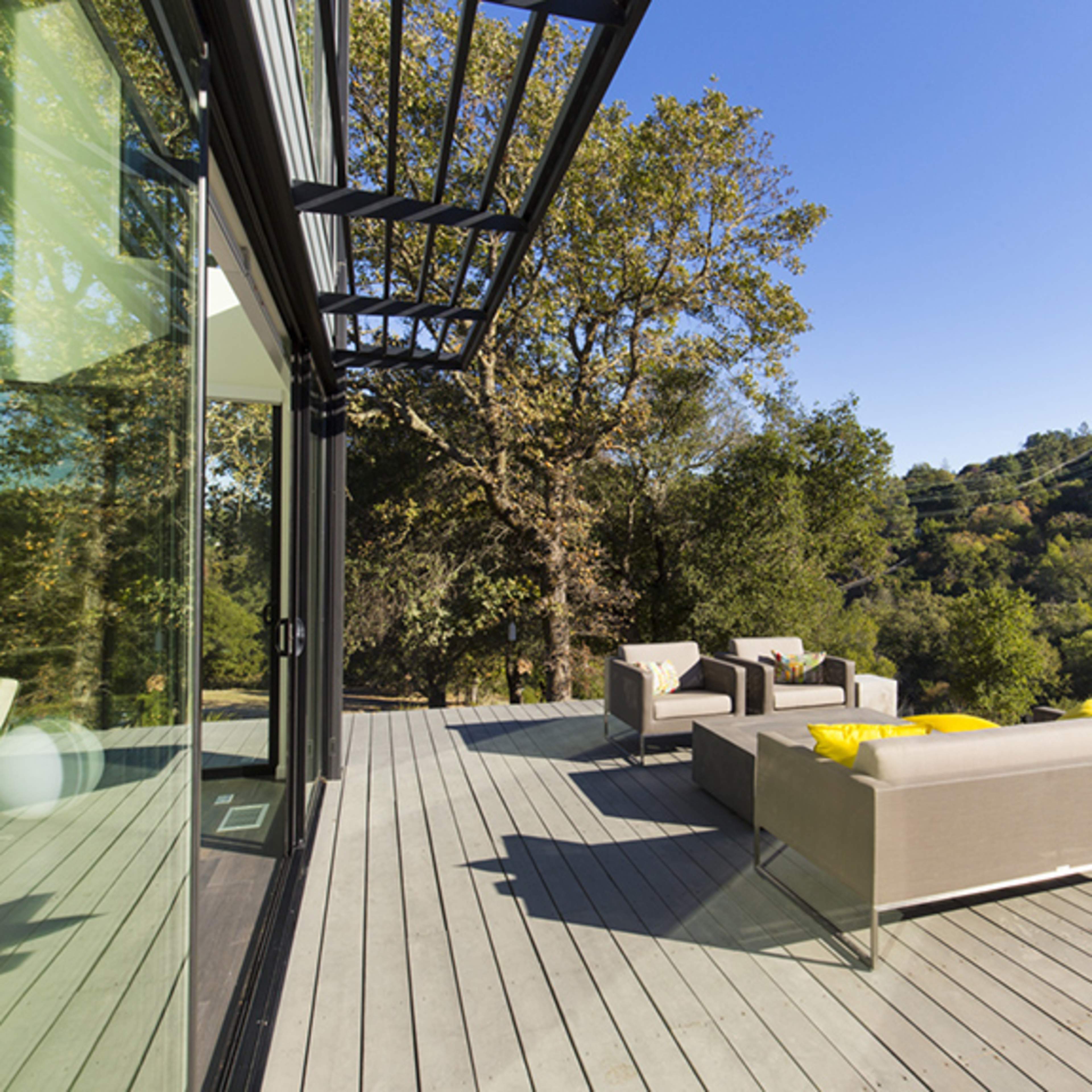 A modern deck features sleek outdoor furniture and overlooks a wooded hillside under a clear blue sky.