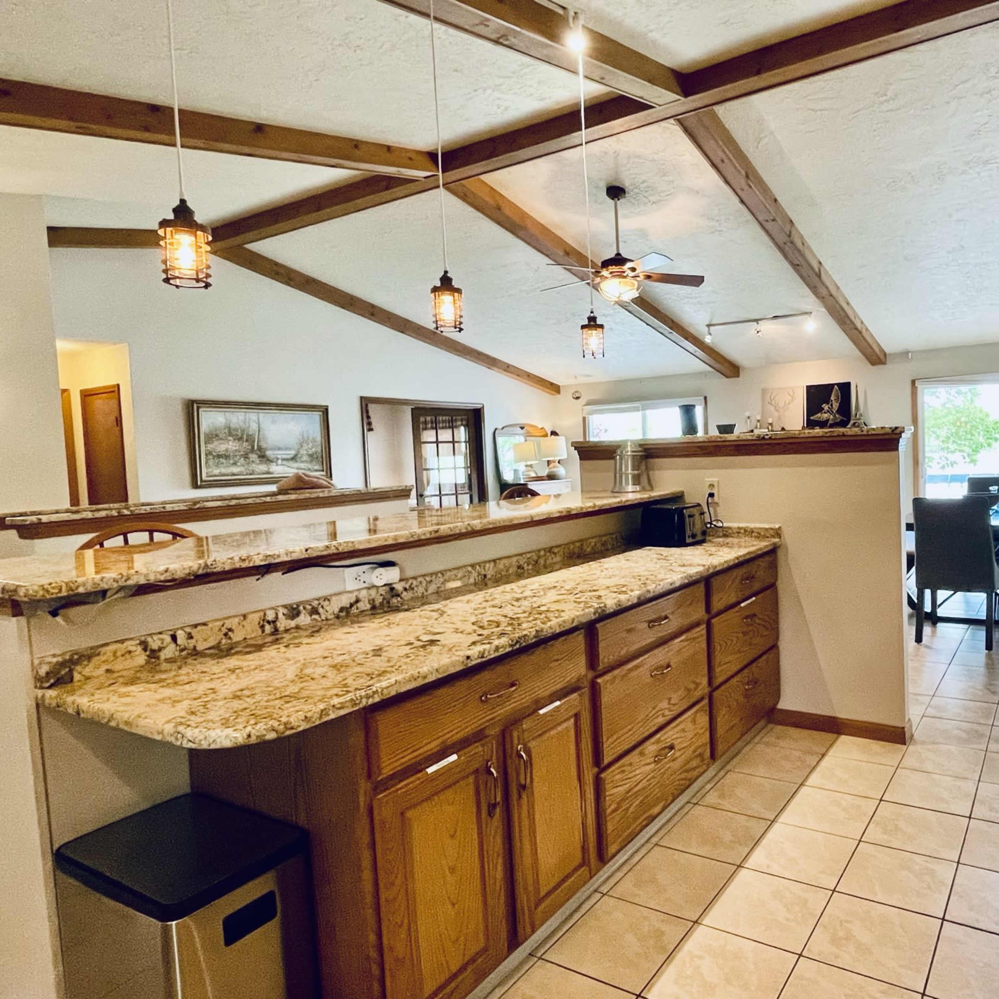 A kitchen with wooden cabinetry, a granite countertop, and an open layout leading to a dining area with a large window.