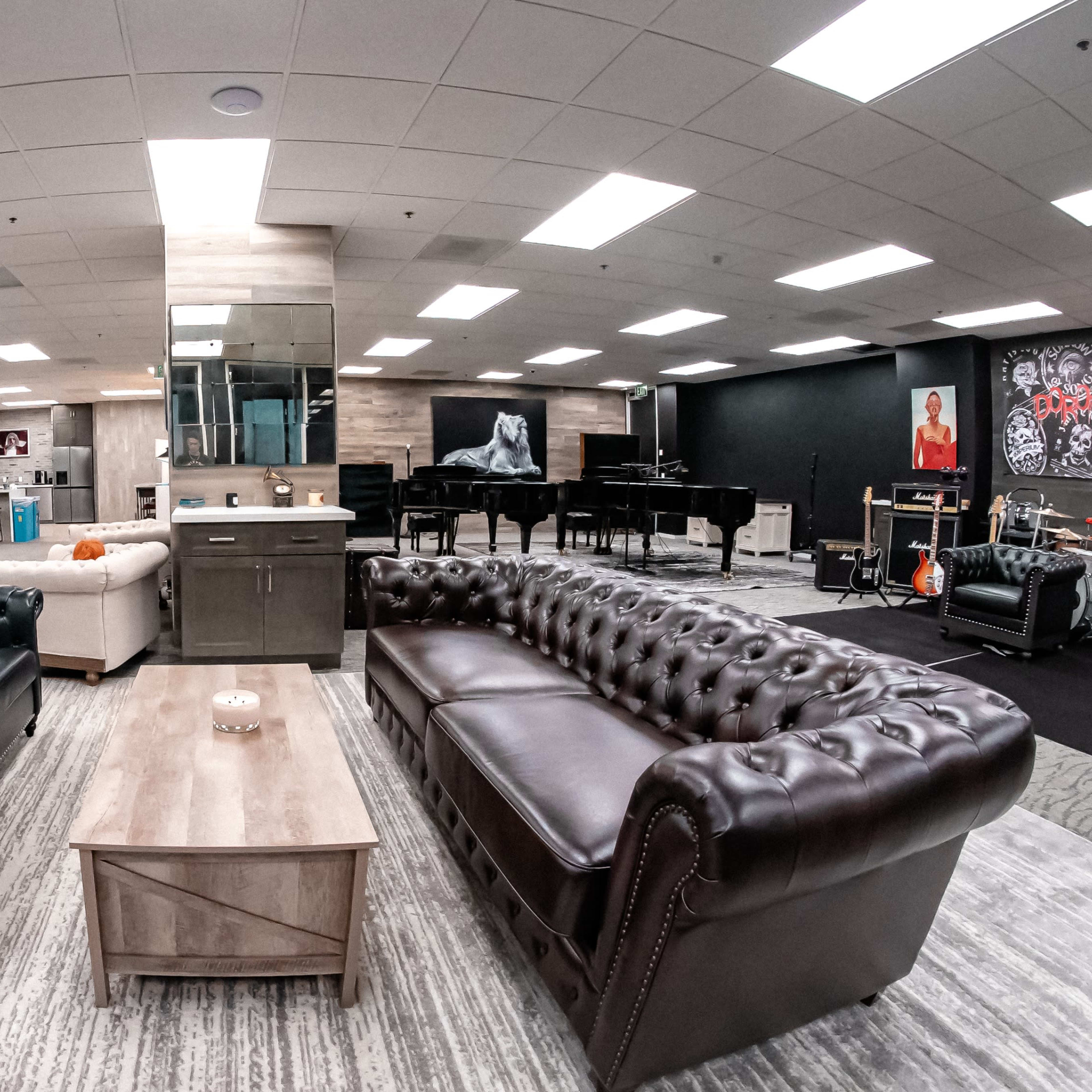 A spacious lounge area featuring two contrasting leather sofas facing a wooden coffee table, surrounded by musical instruments and artwork on the walls.