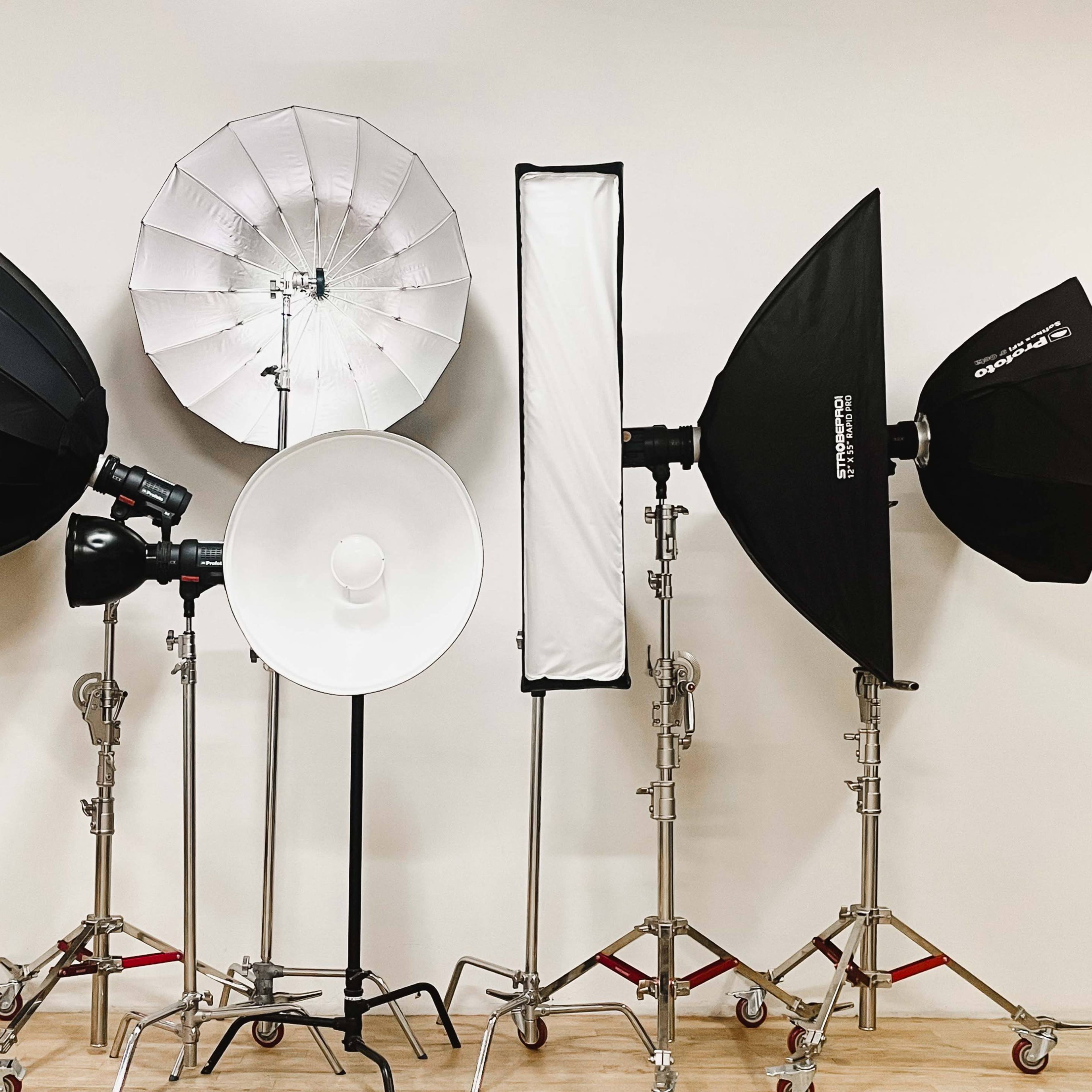 A collection of studio lighting equipment arranged on stands against a plain wall.