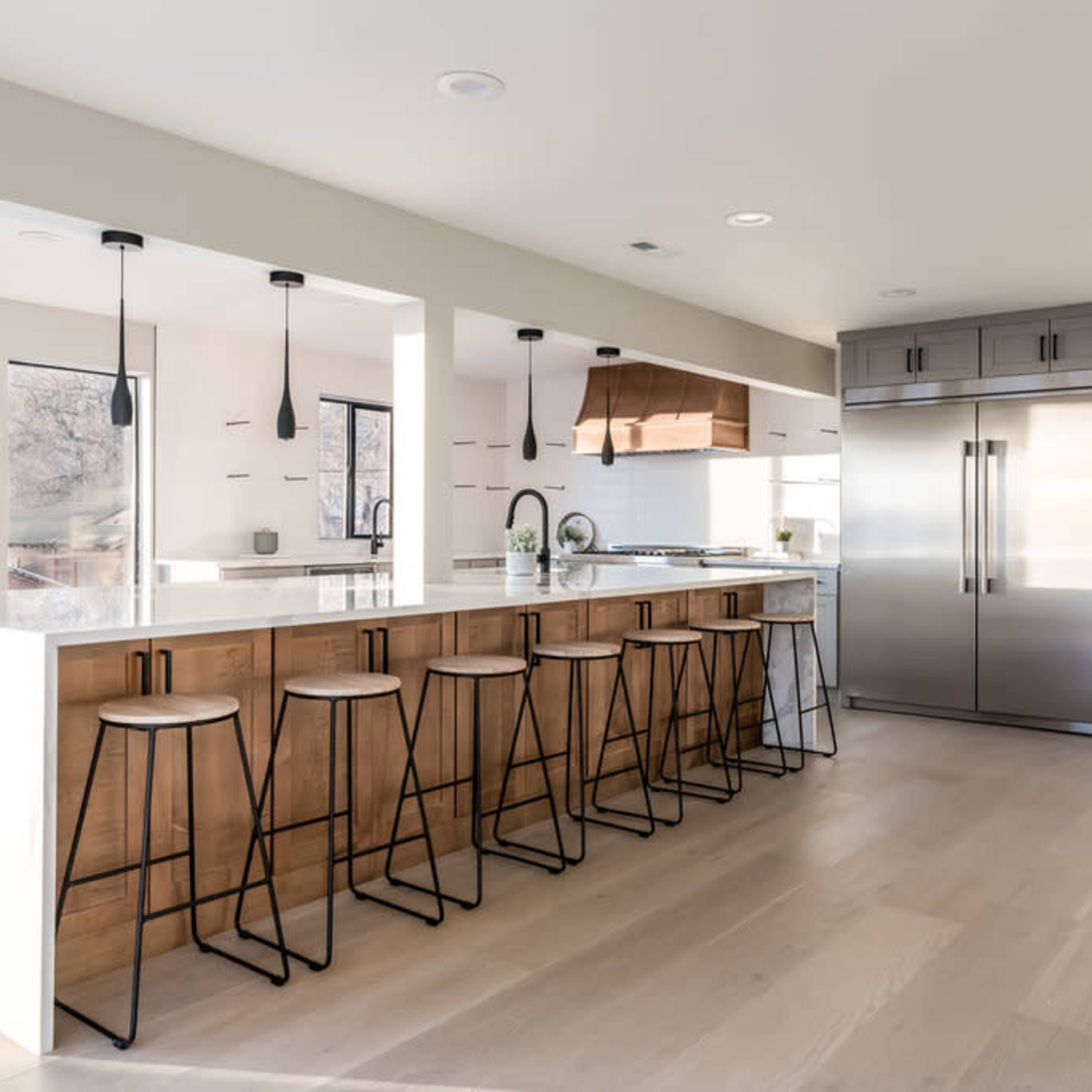 A modern kitchen featuring a large island with high stools, stainless steel appliances, and a light color palette.