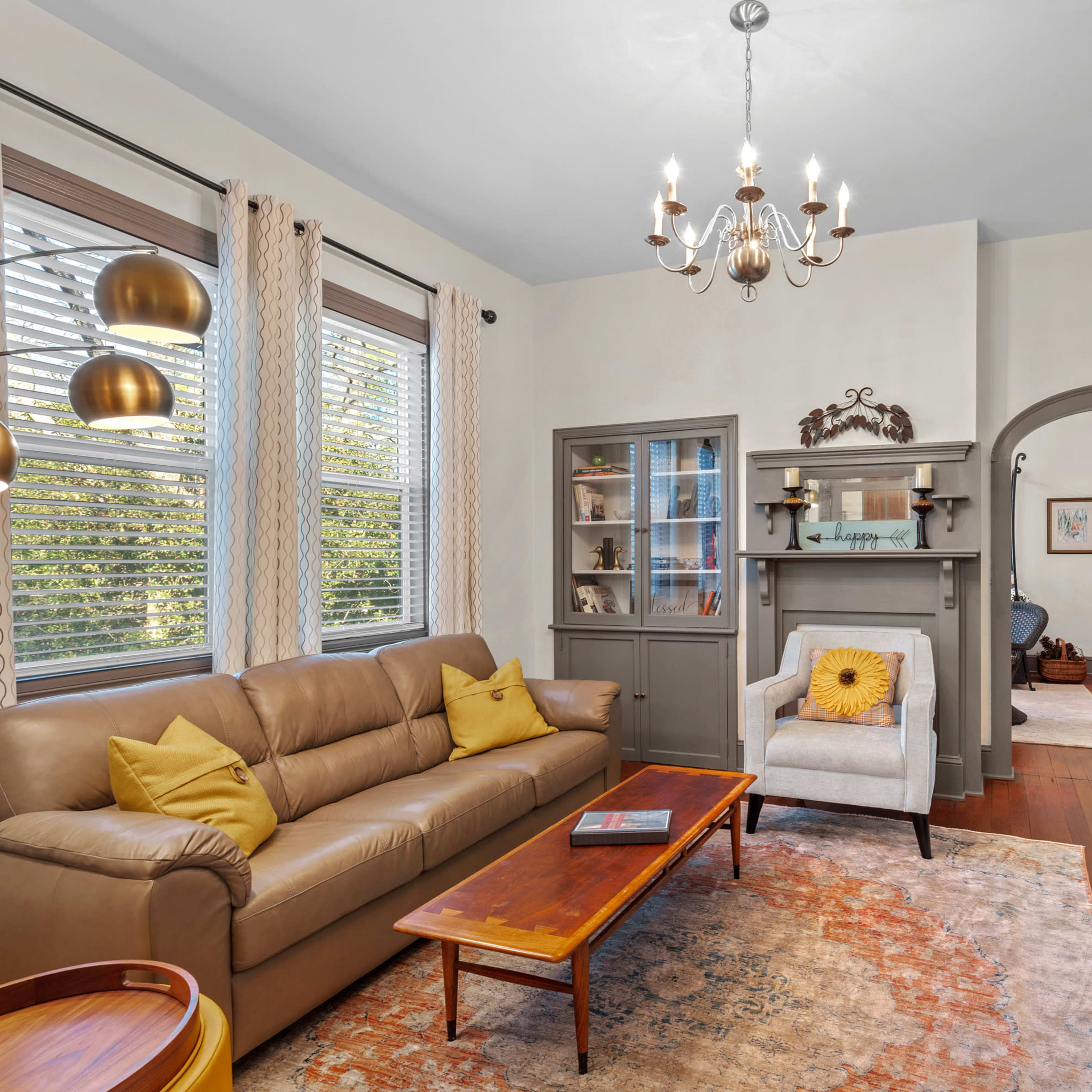 The living room features a beige leather sofa, a wooden coffee table, and a decorative fireplace, with natural light coming through the windows.