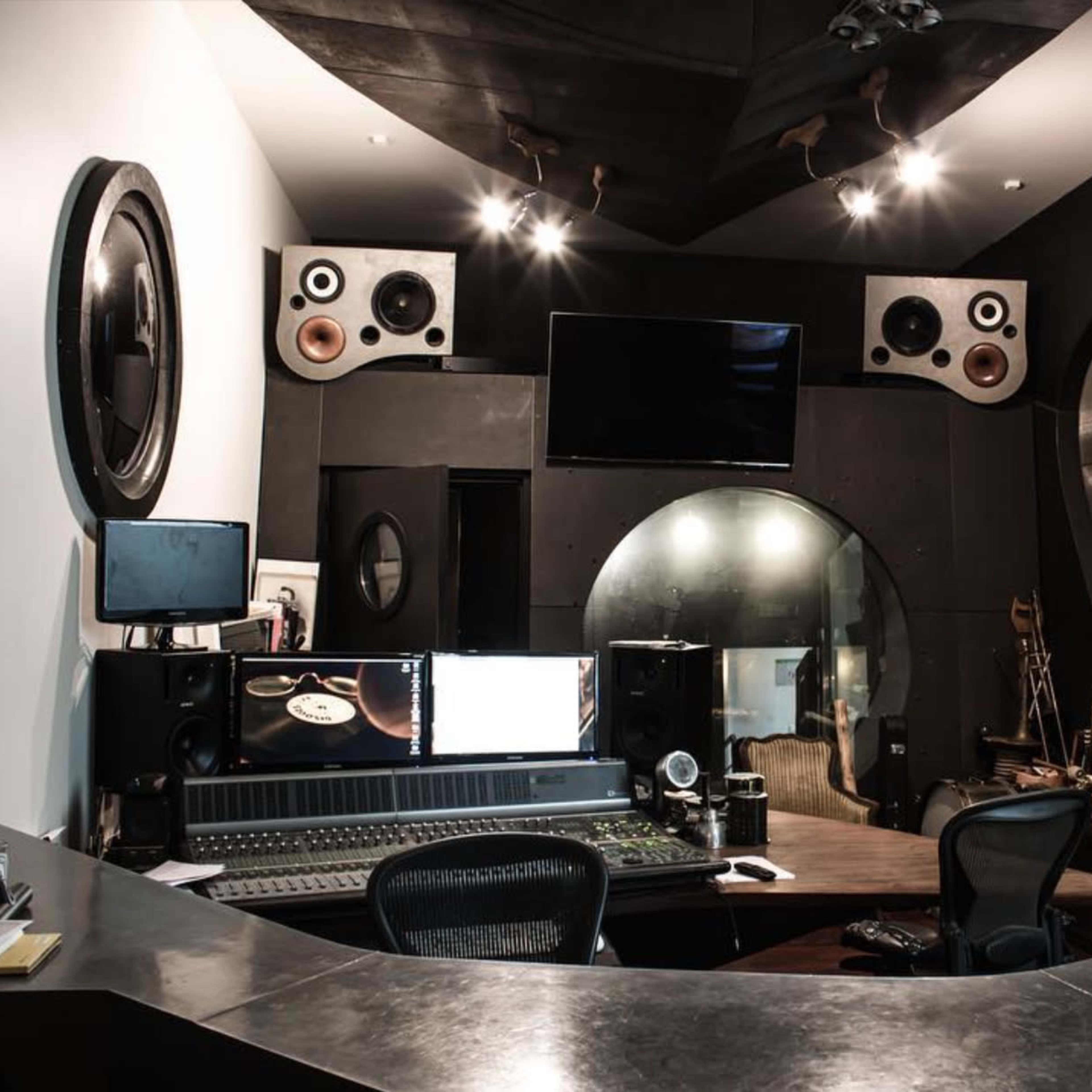 A modern recording studio with sound equipment, large speakers, and a control desk in a dimly lit space.