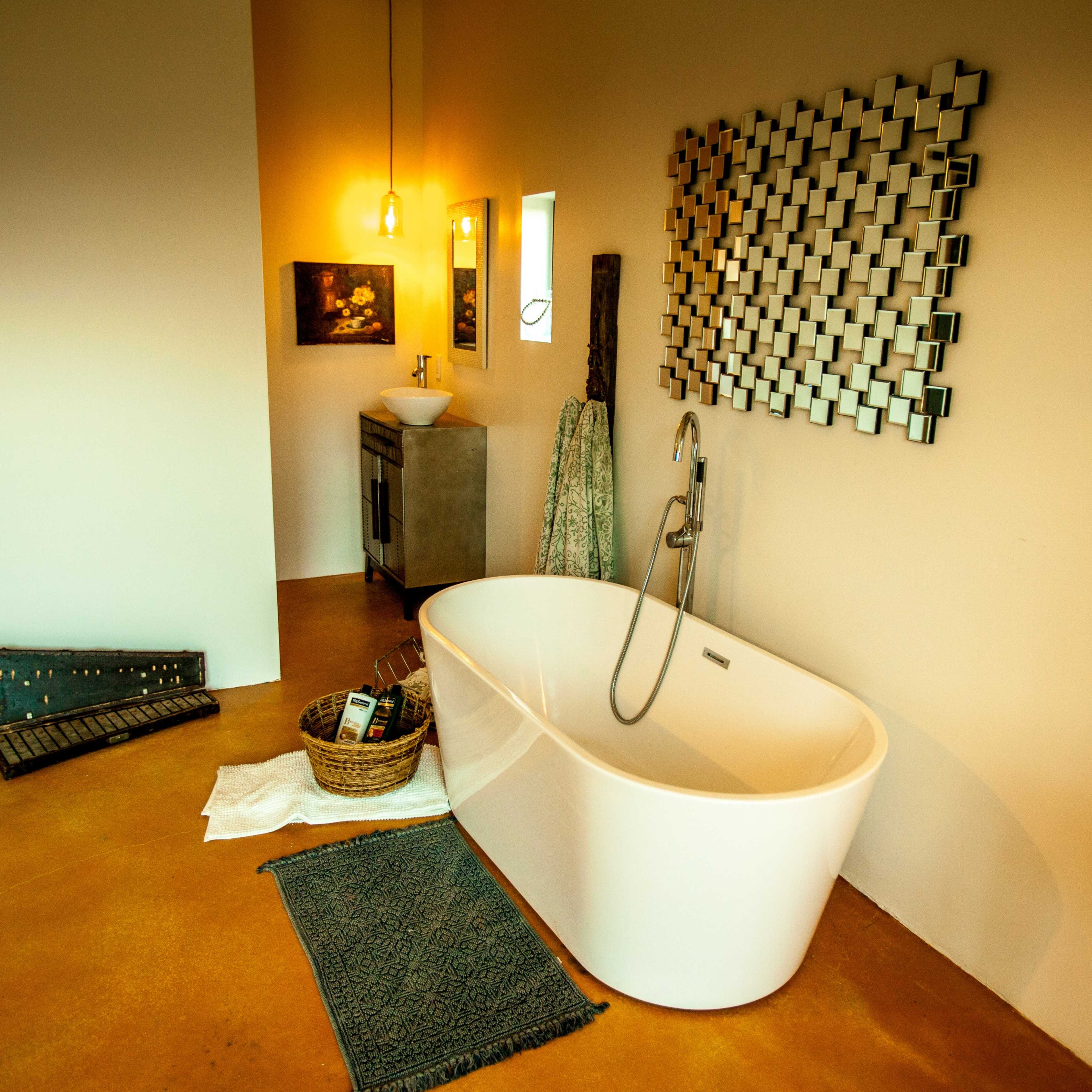 A modern bathroom features a freestanding white bathtub, a woven basket, and a decorative wall mirror.