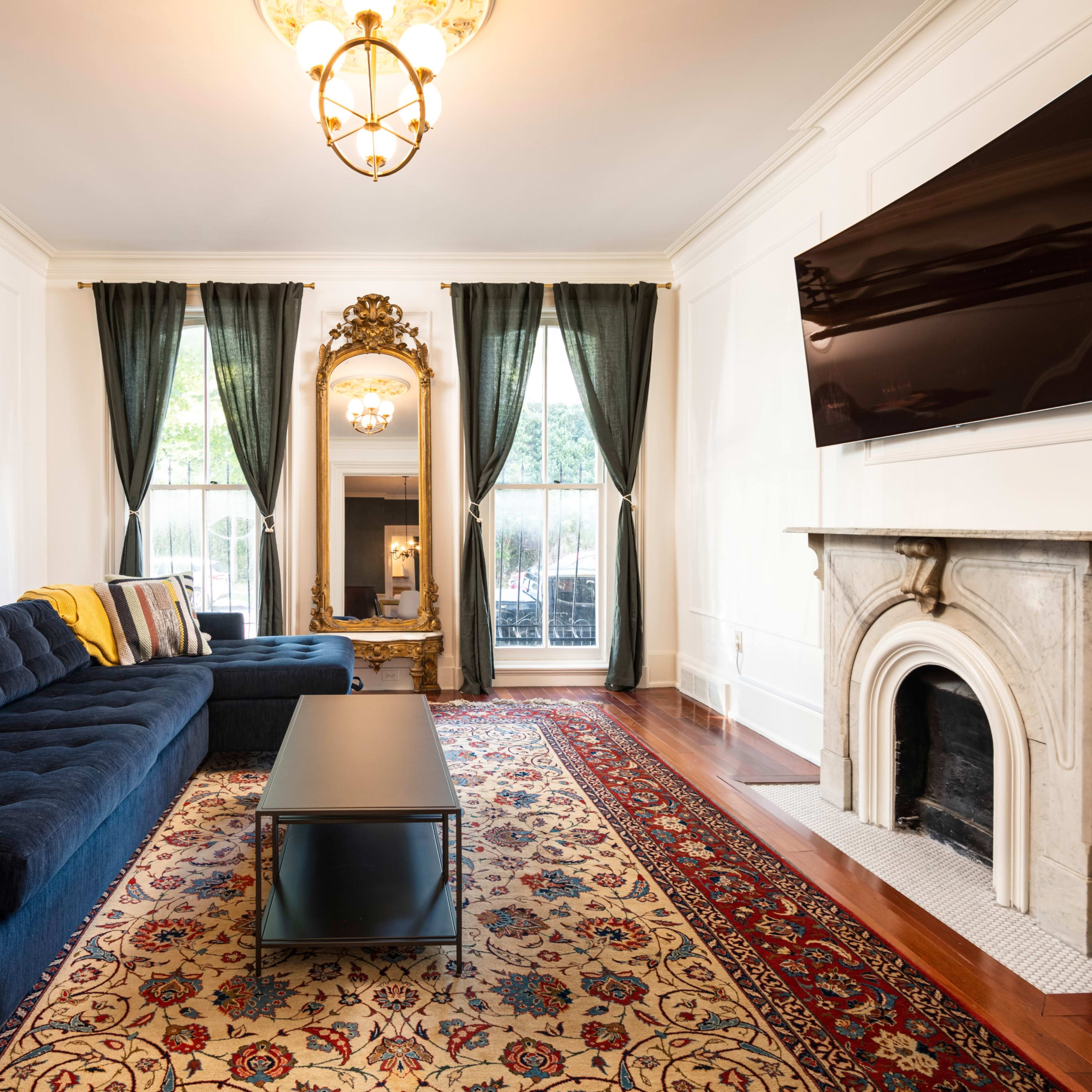 A contemporary living room featuring a blue sofa, a dark coffee table, and a decorative rug, with large windows dressed in green curtains.