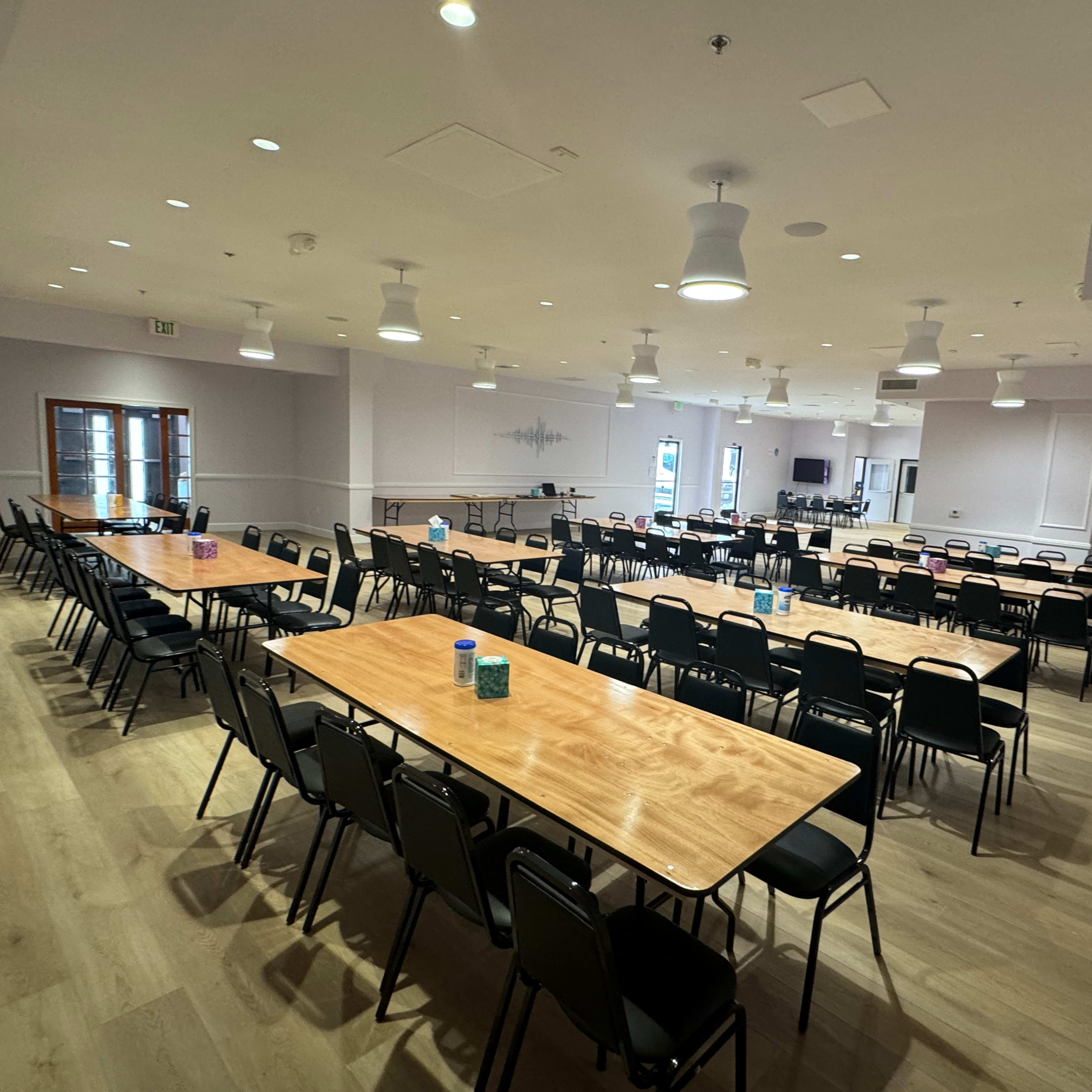 A large, empty meeting room with multiple rows of tables and chairs arranged for an event.
