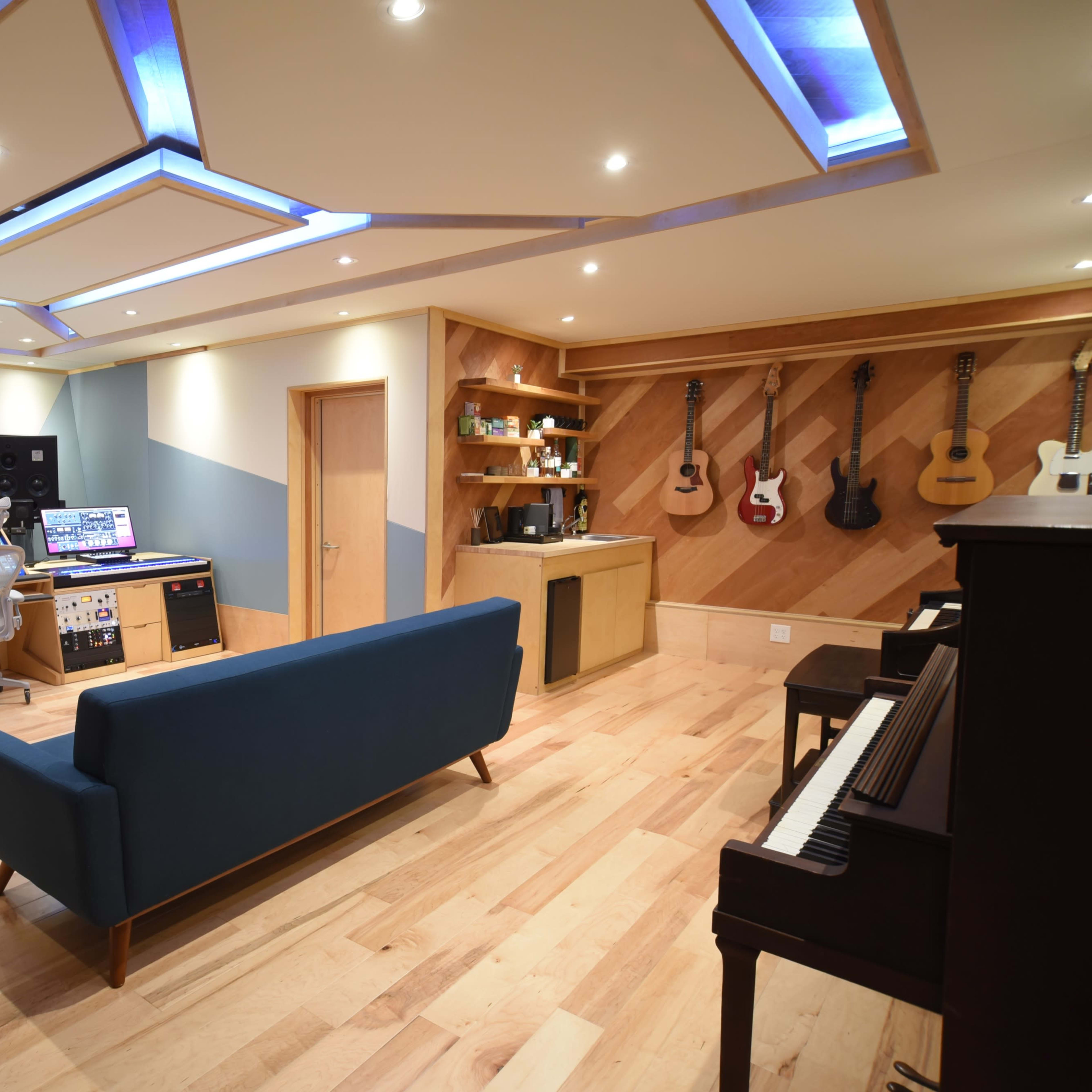 A modern music studio features a mixing console, acoustic treatment, and various musical instruments displayed on the wall.