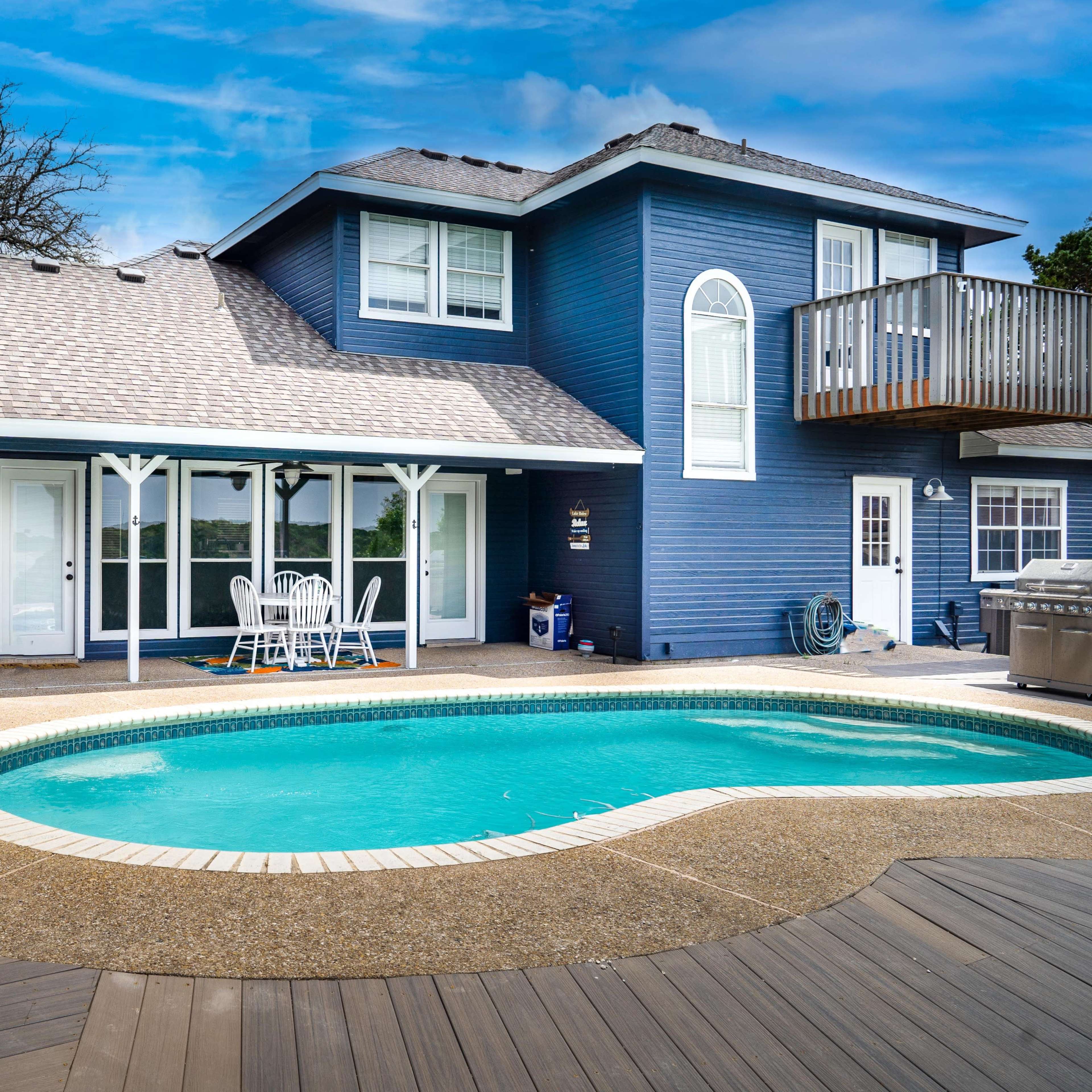 A blue two-story house with a pool and wooden deck is seen in the backyard.