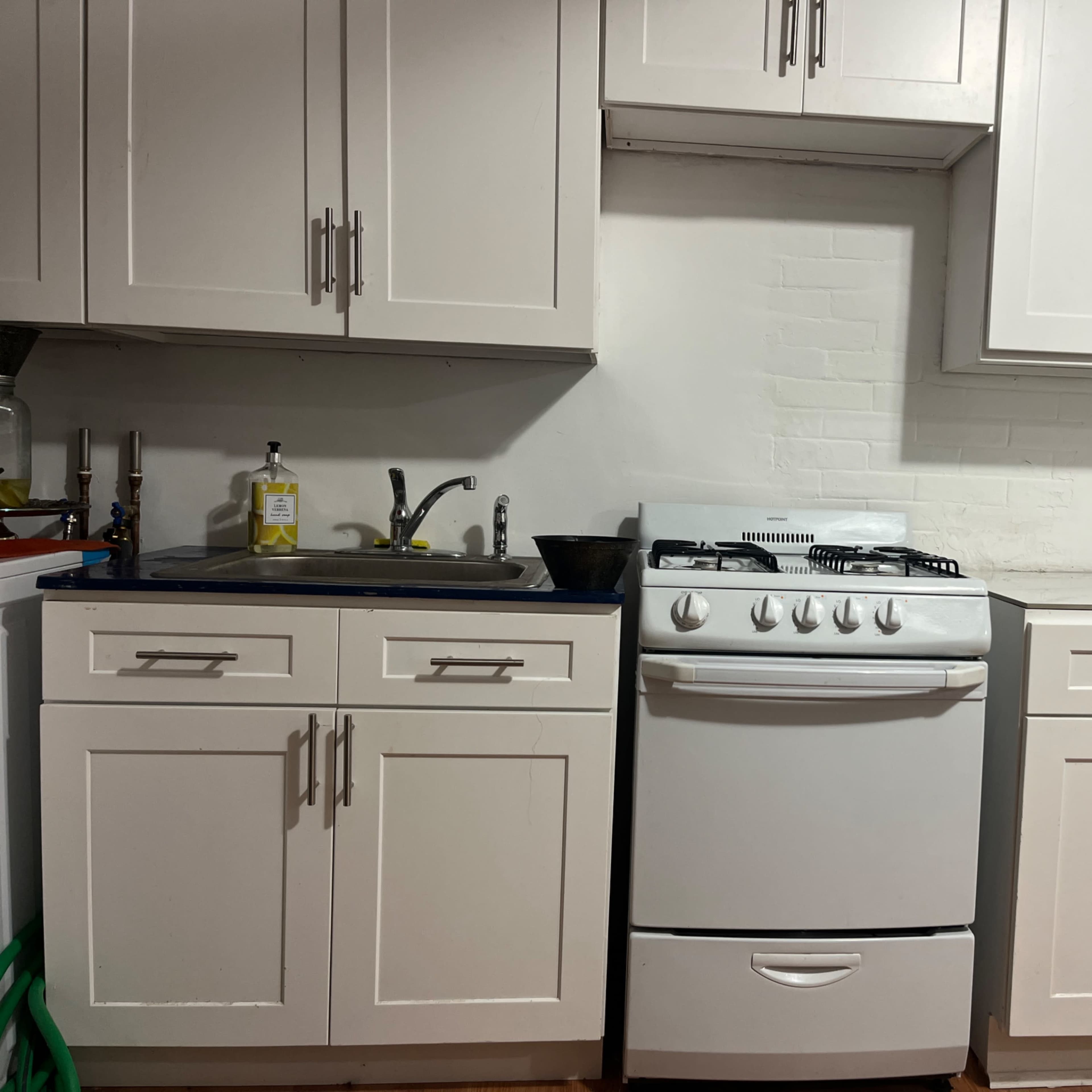 A clean kitchen with white cabinets, a stove in the center, and a sink beside it.