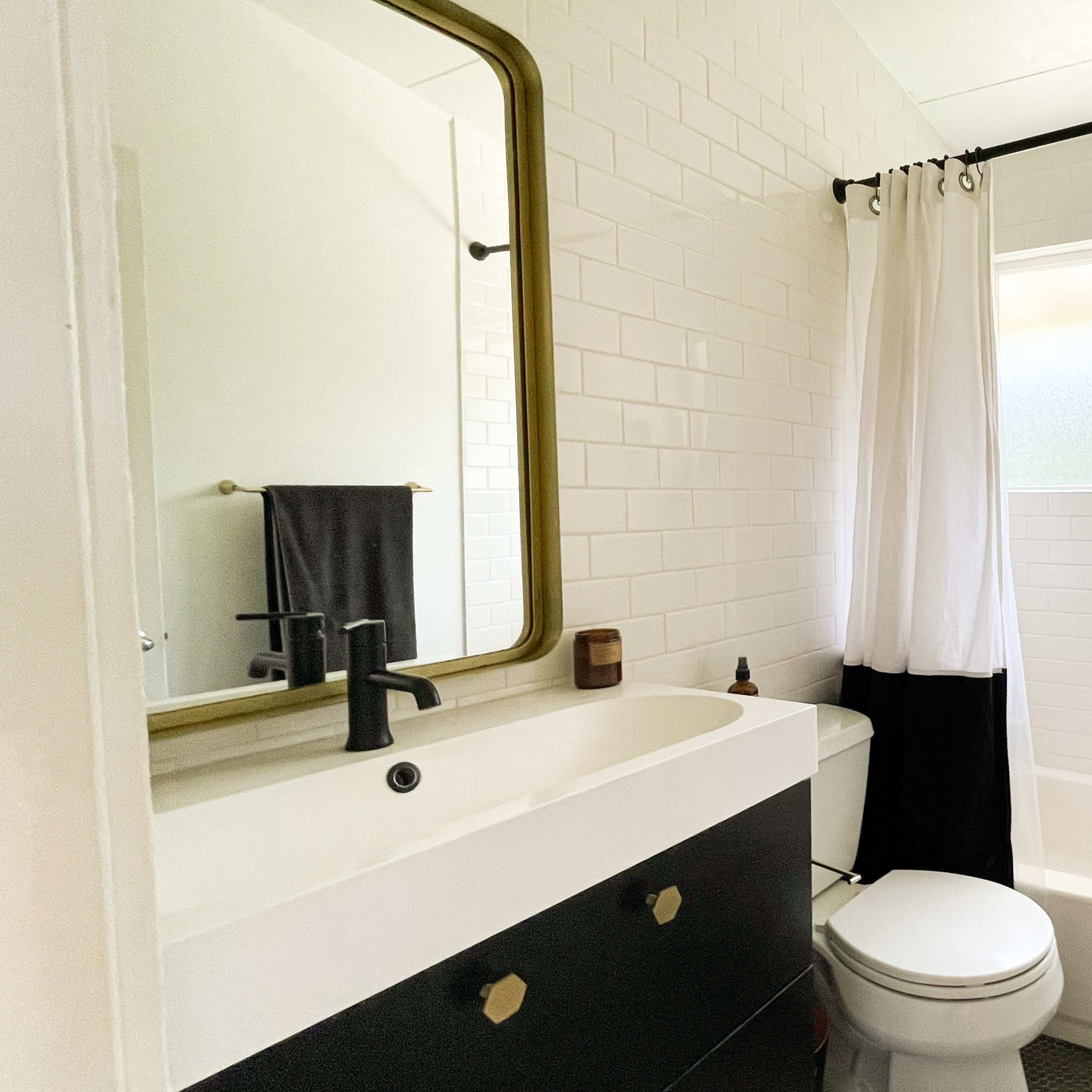 A modern bathroom with a white tiled shower area, a black and white color scheme, a large mirror, and a window for natural light.