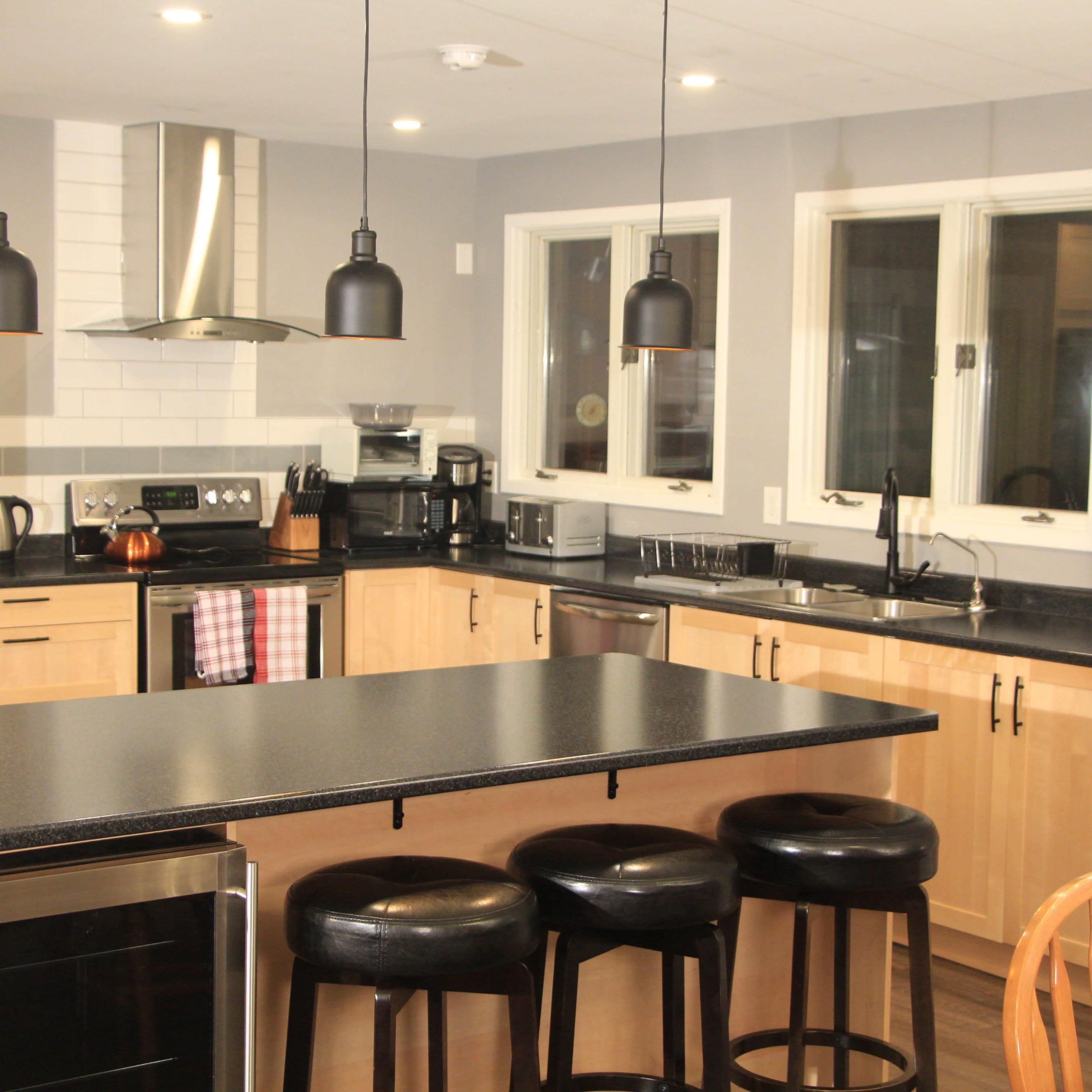 A modern kitchen featuring light wood cabinets, a black countertop, and a central island with seating for four.