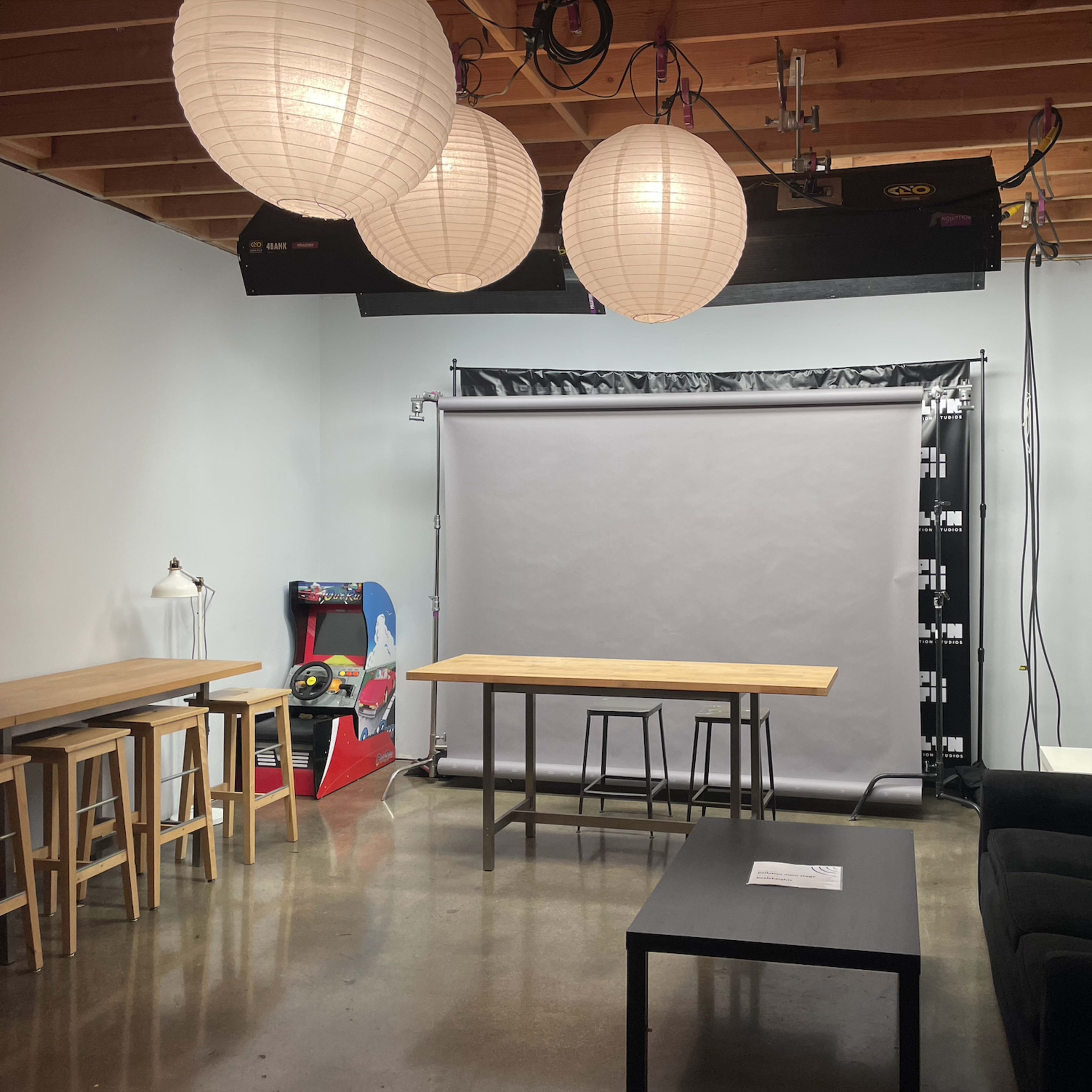 A studio space with a gray backdrop, wooden tables, a couch, and hanging paper lanterns.