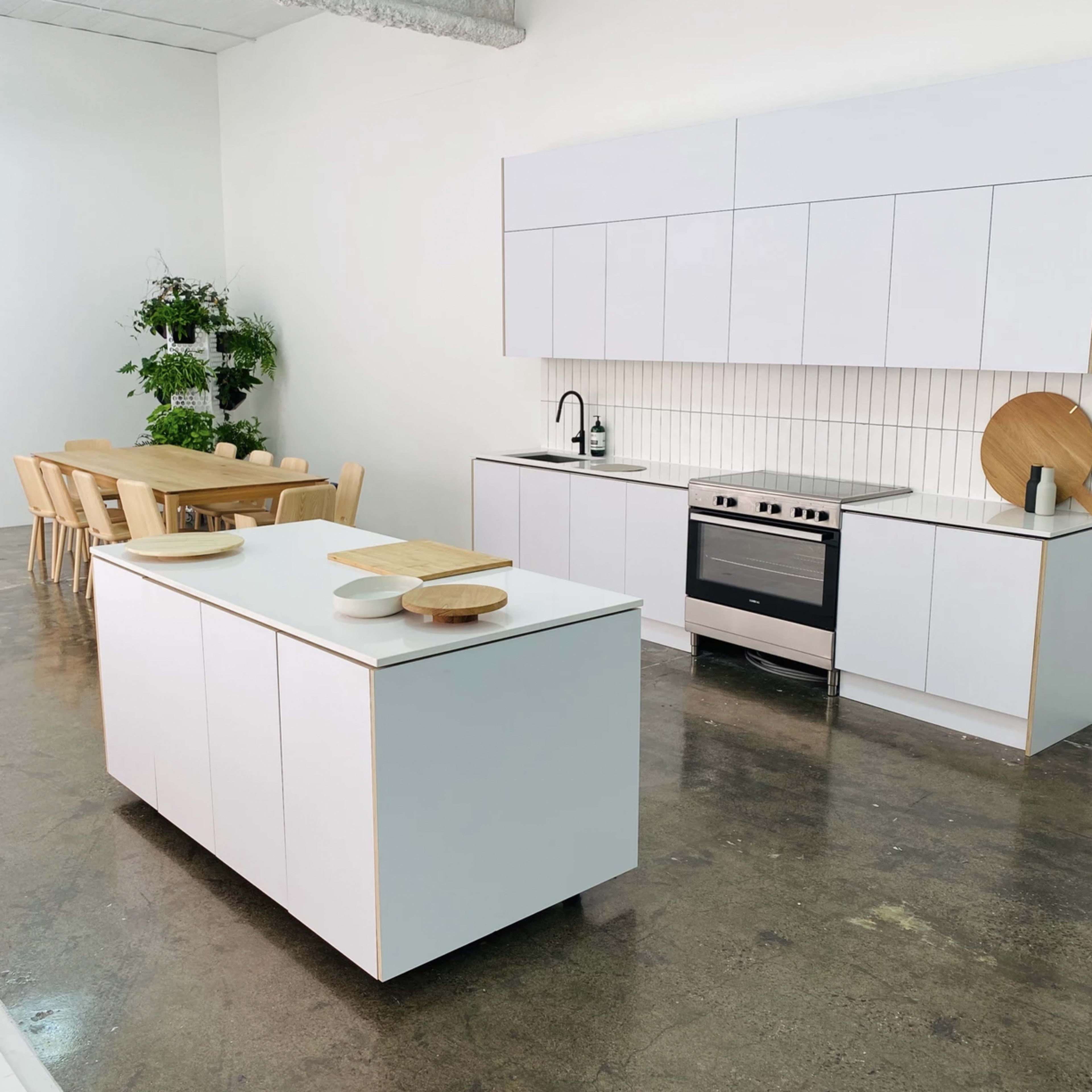 A modern kitchen with a white cabinetry setup, an island in the center, a stainless steel oven, and a dining table with wooden chairs.