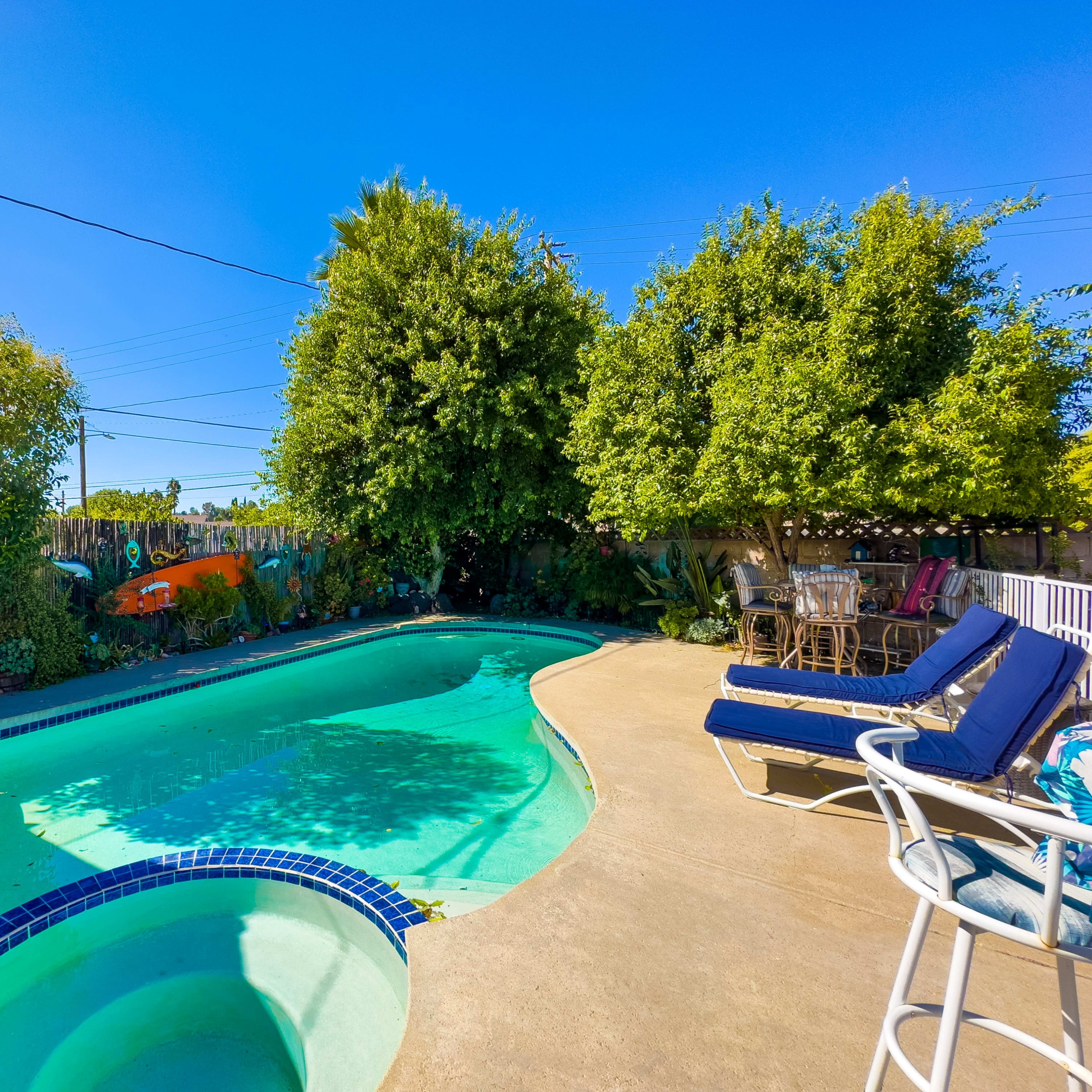 A residential backyard with a swimming pool surrounded by greenery and a seating area.