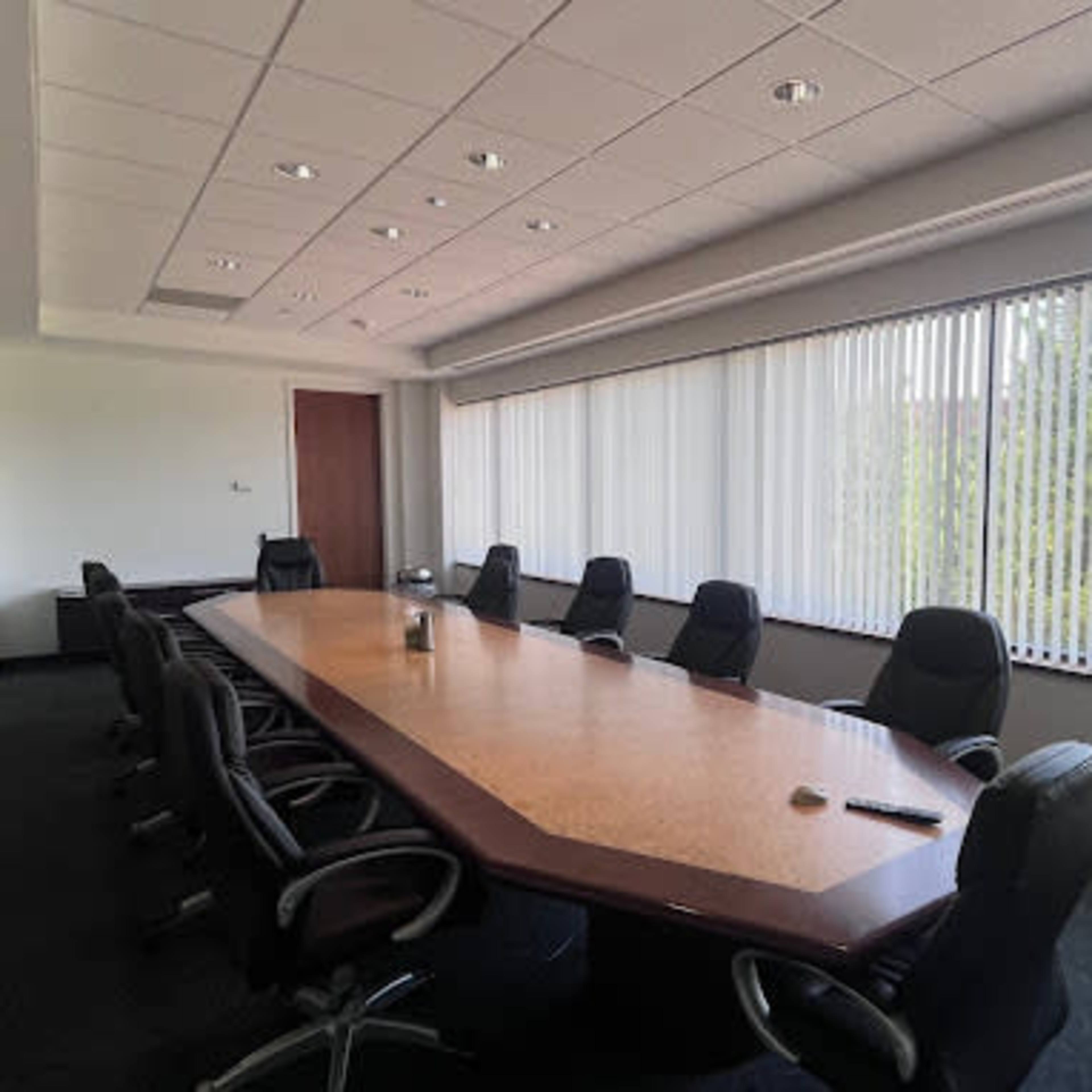 A conference room features a long table surrounded by black office chairs, with large windows allowing natural light to fill the space.
