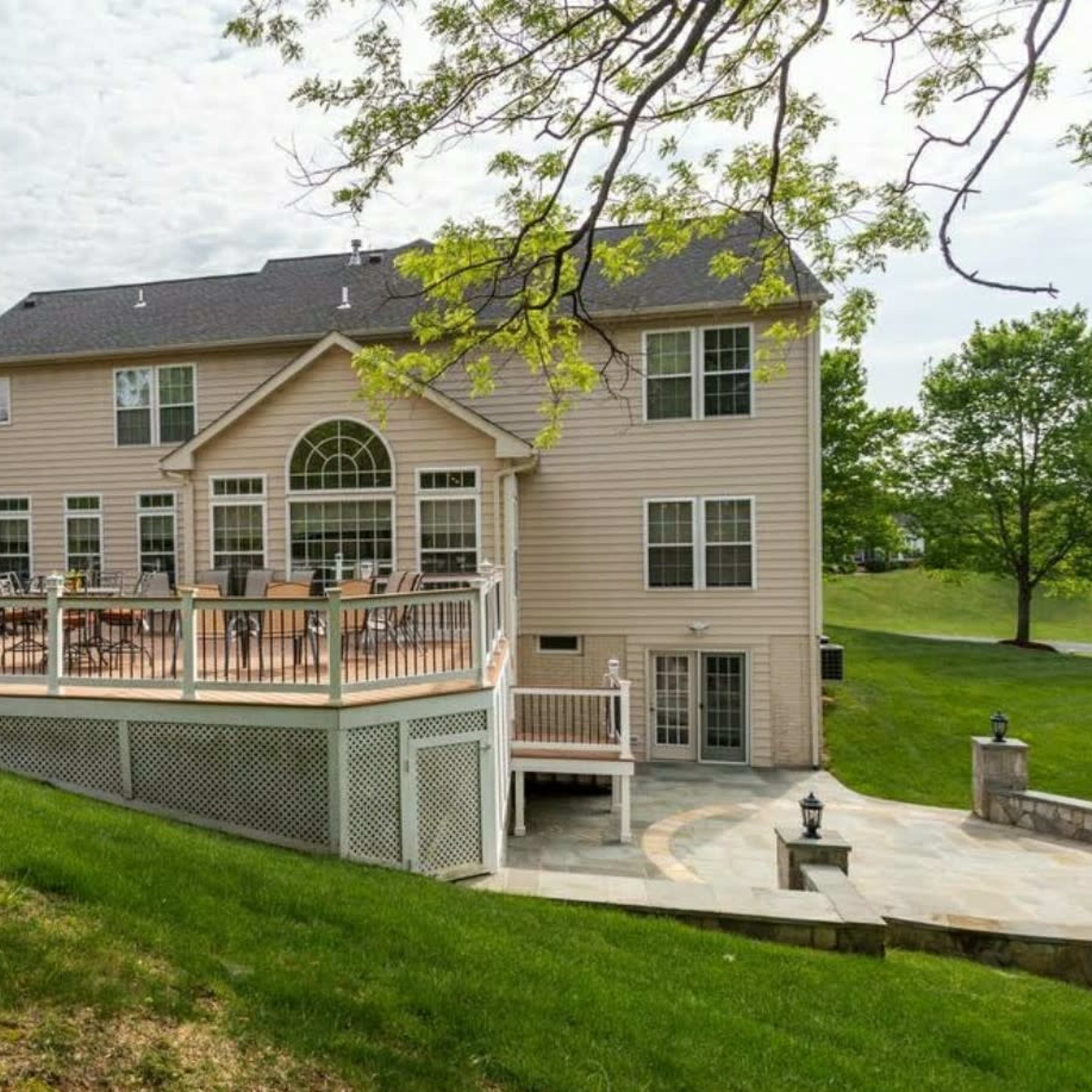 A large two-story house with a deck overlooking a grassy area.