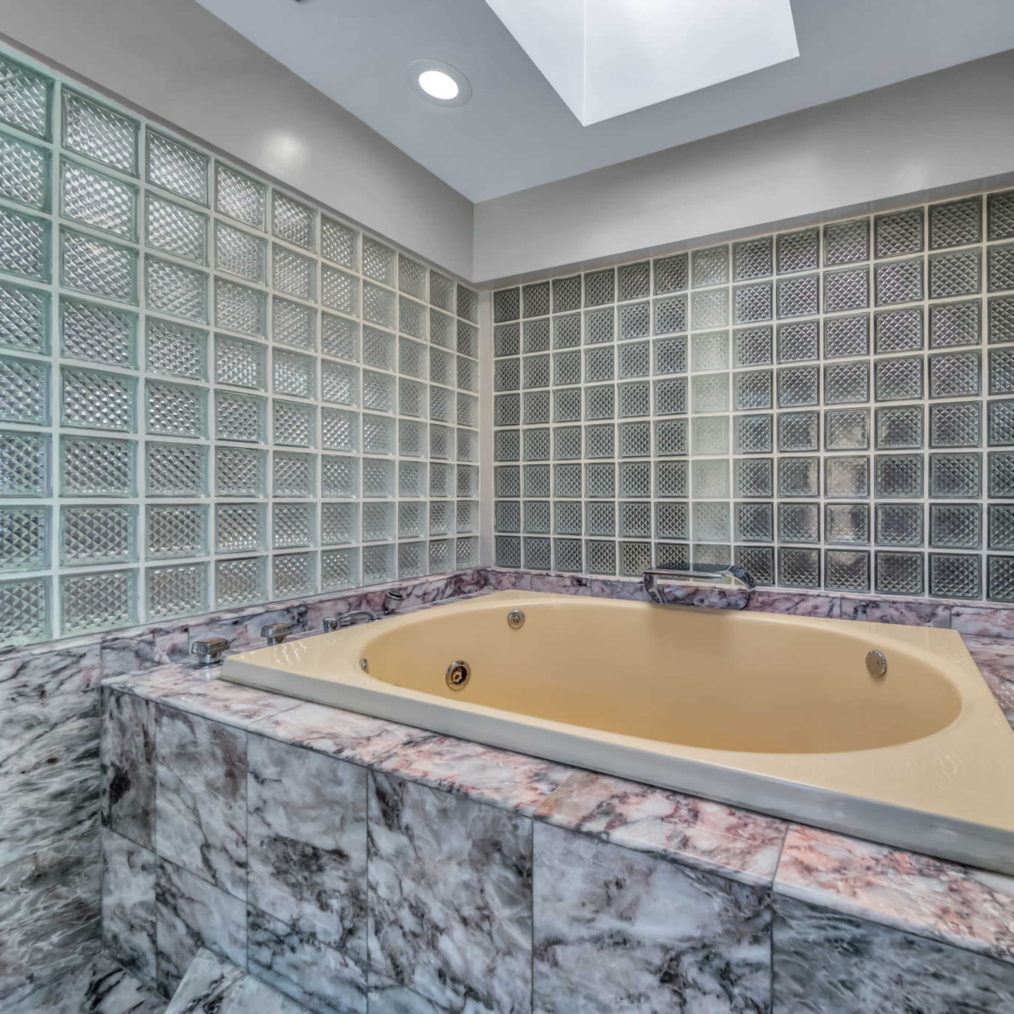 A corner bathtub surrounded by glass block walls and marble tiling.