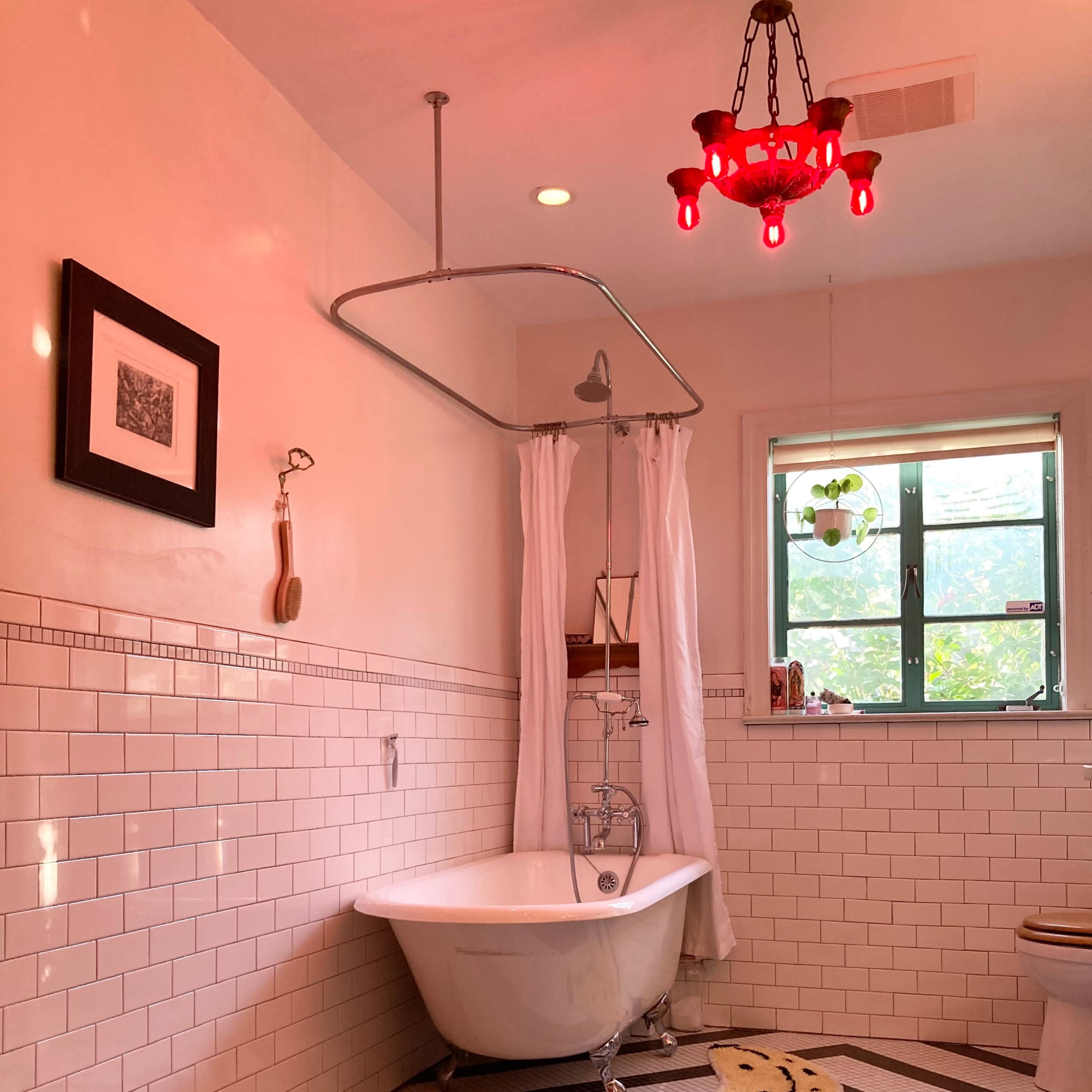 A bathroom features a clawfoot tub, a shower with white curtains, decorative tile flooring in a geometric pattern, and a red chandelier.