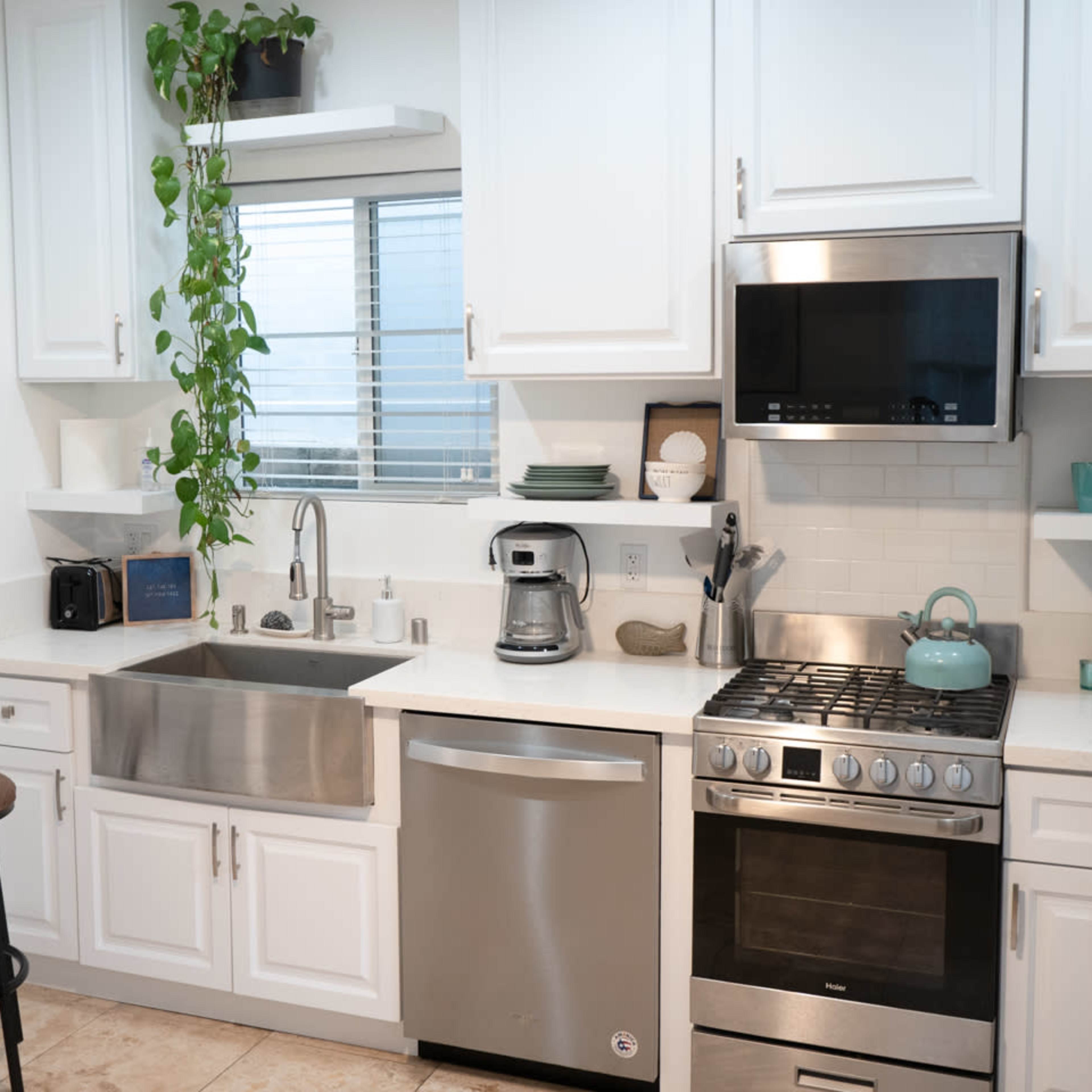 A modern kitchen featuring stainless steel appliances, white cabinetry, and a sink with a view to a small window.