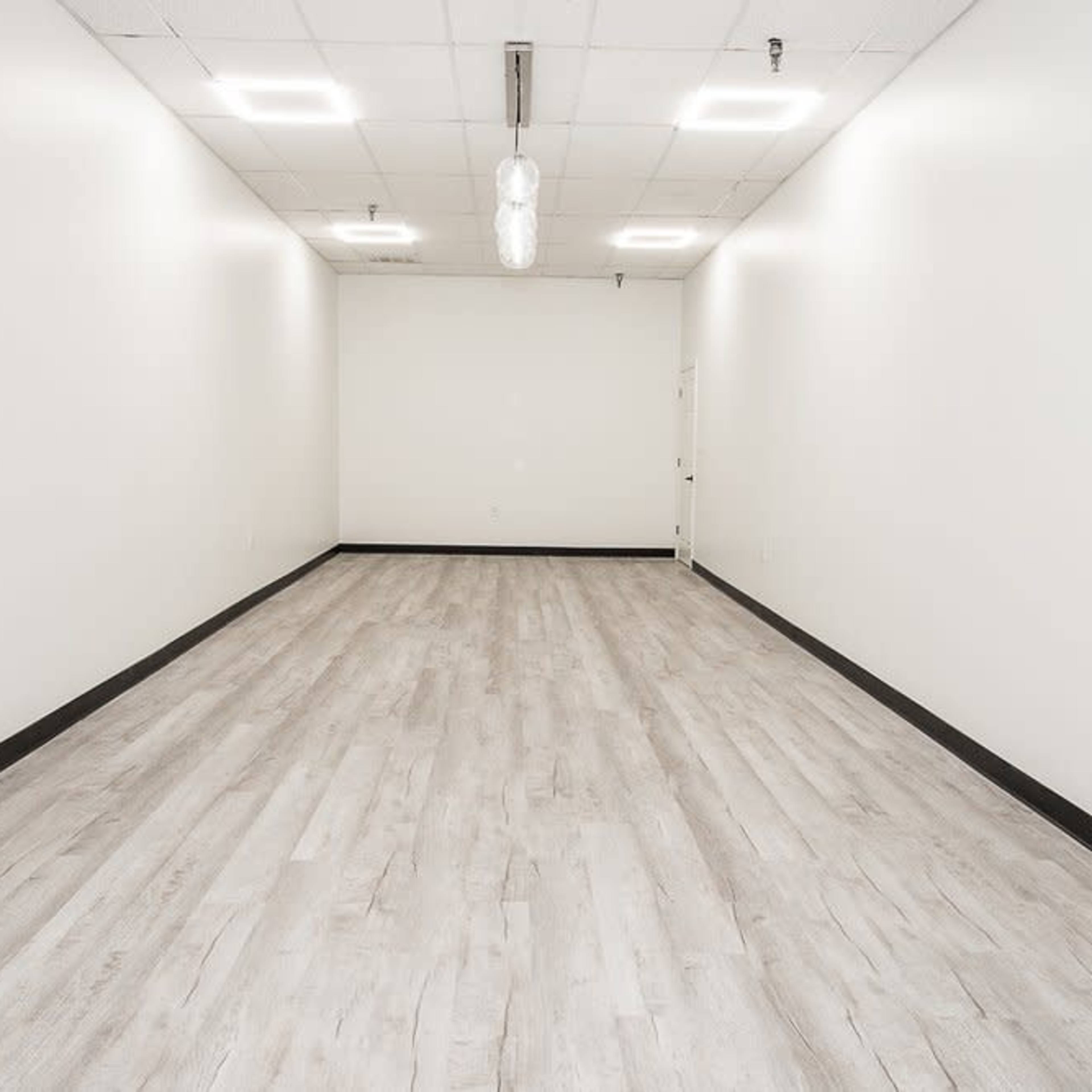 An empty, well-lit room with light-colored wooden flooring and white walls.