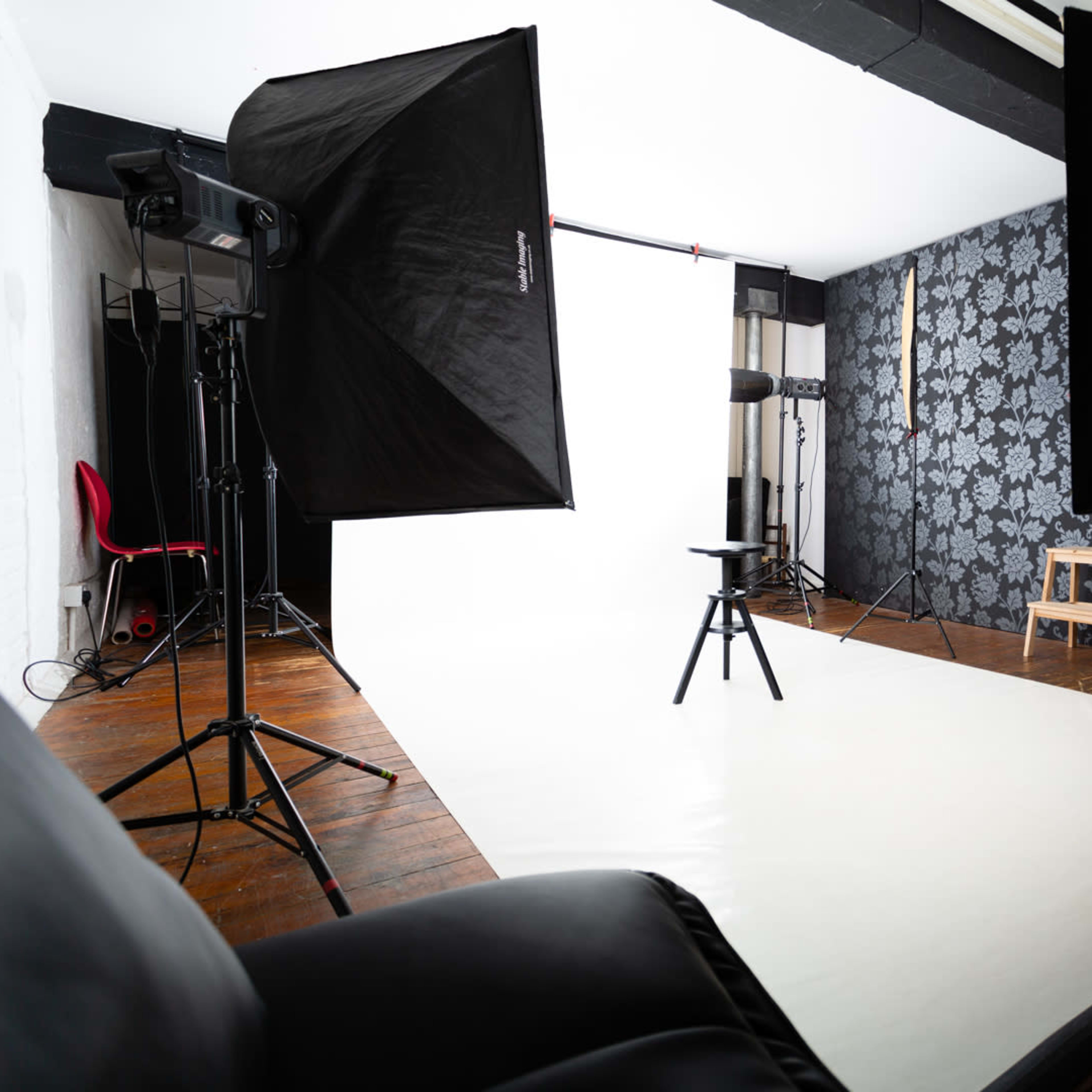 A photography studio setup with softbox lights, a backdrop, a stool in the center, and a dark-patterned wall in the background.
