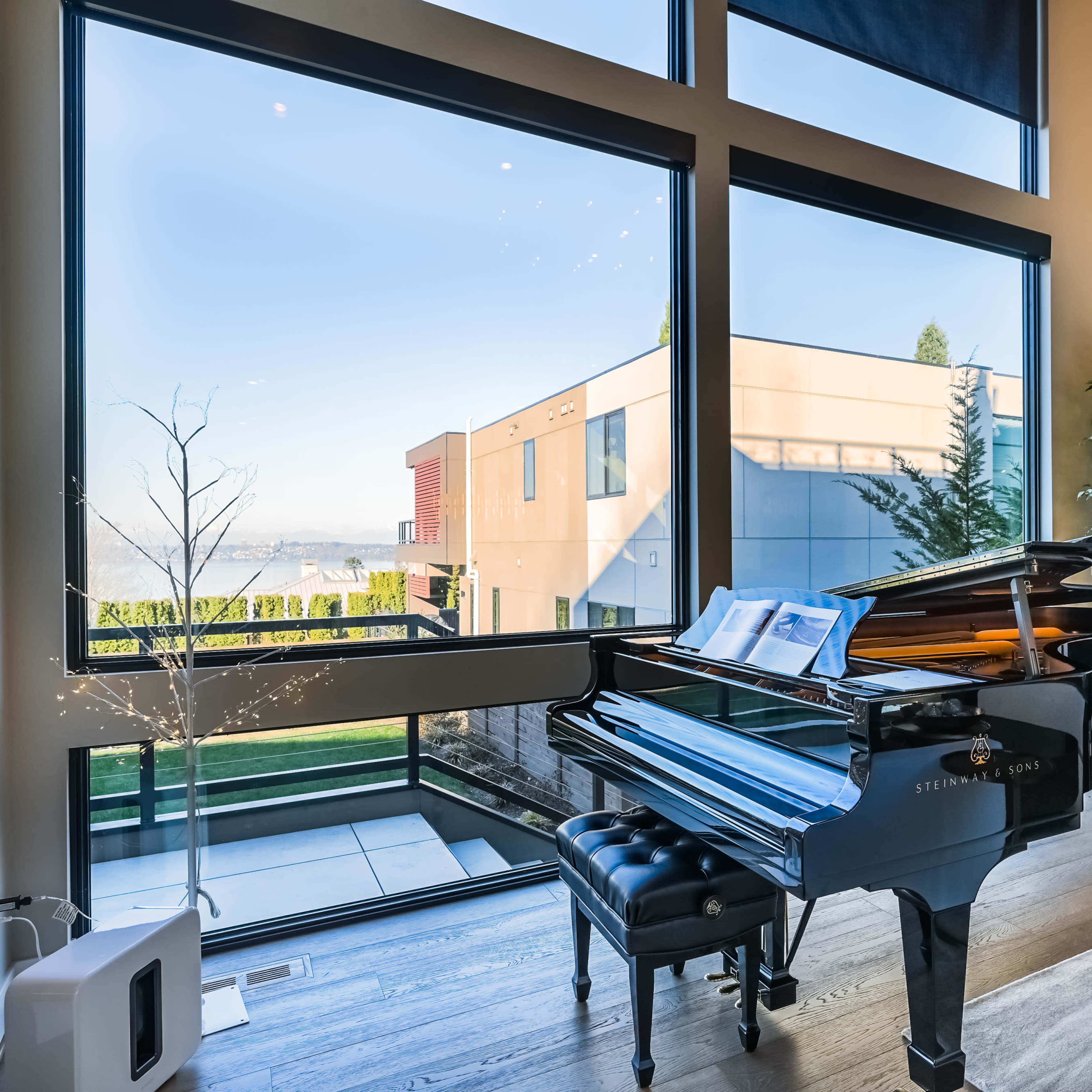 A grand piano sits beside large windows that overlook a landscaped outdoor area.