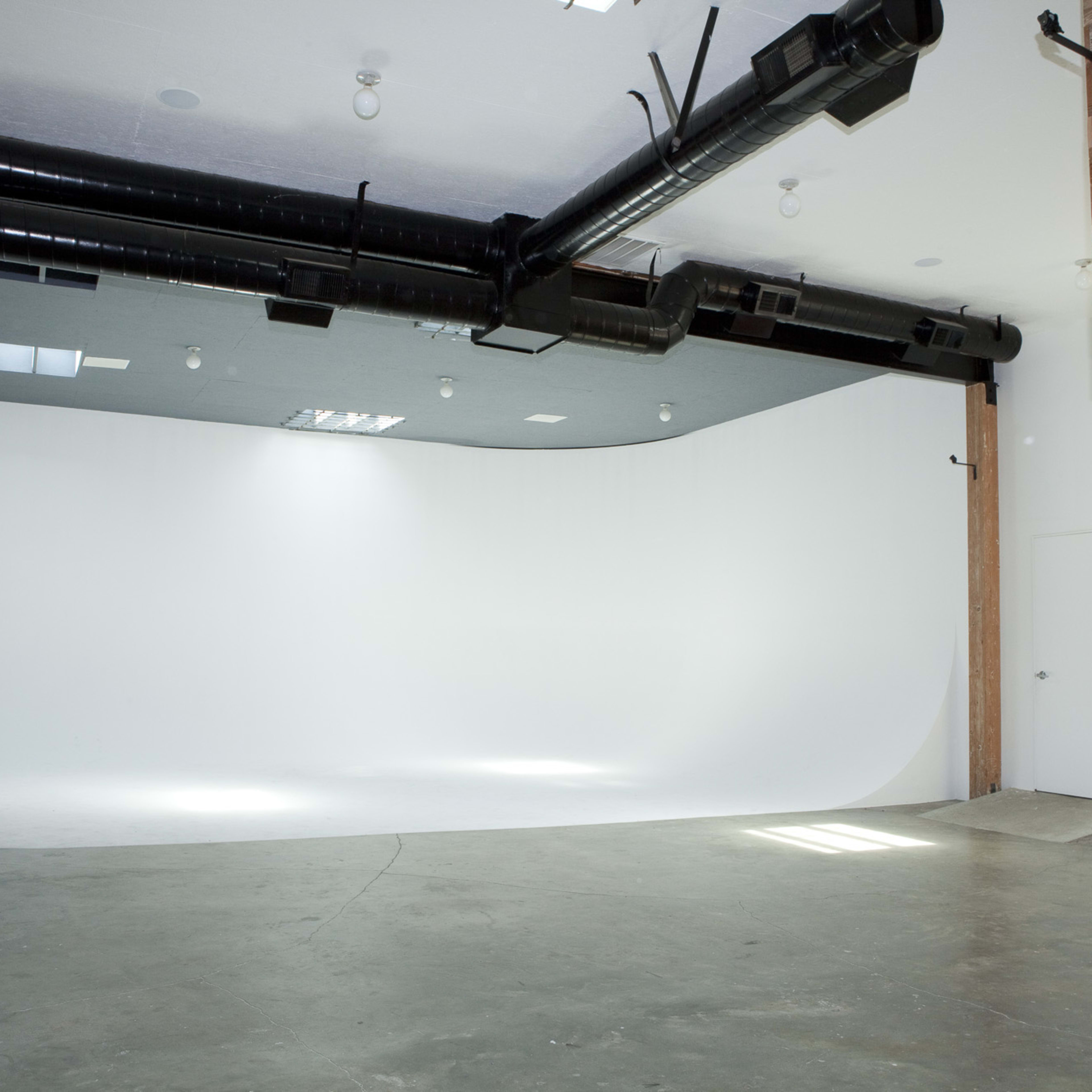 A spacious, empty studio with a white backdrop and industrial-style features, including exposed pipes and wooden elements.