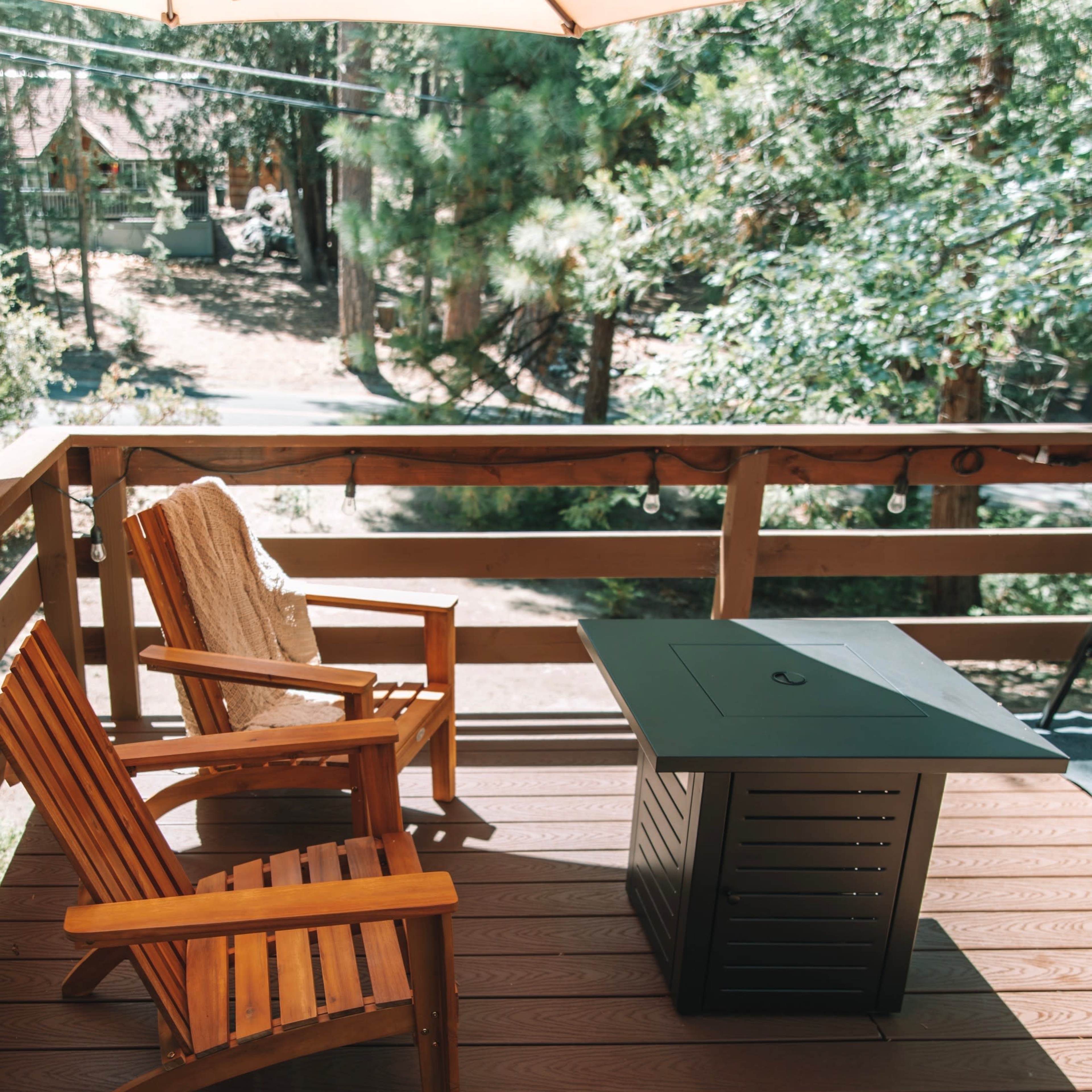 A wooden deck features two chairs and a table, surrounded by trees and a pathway.