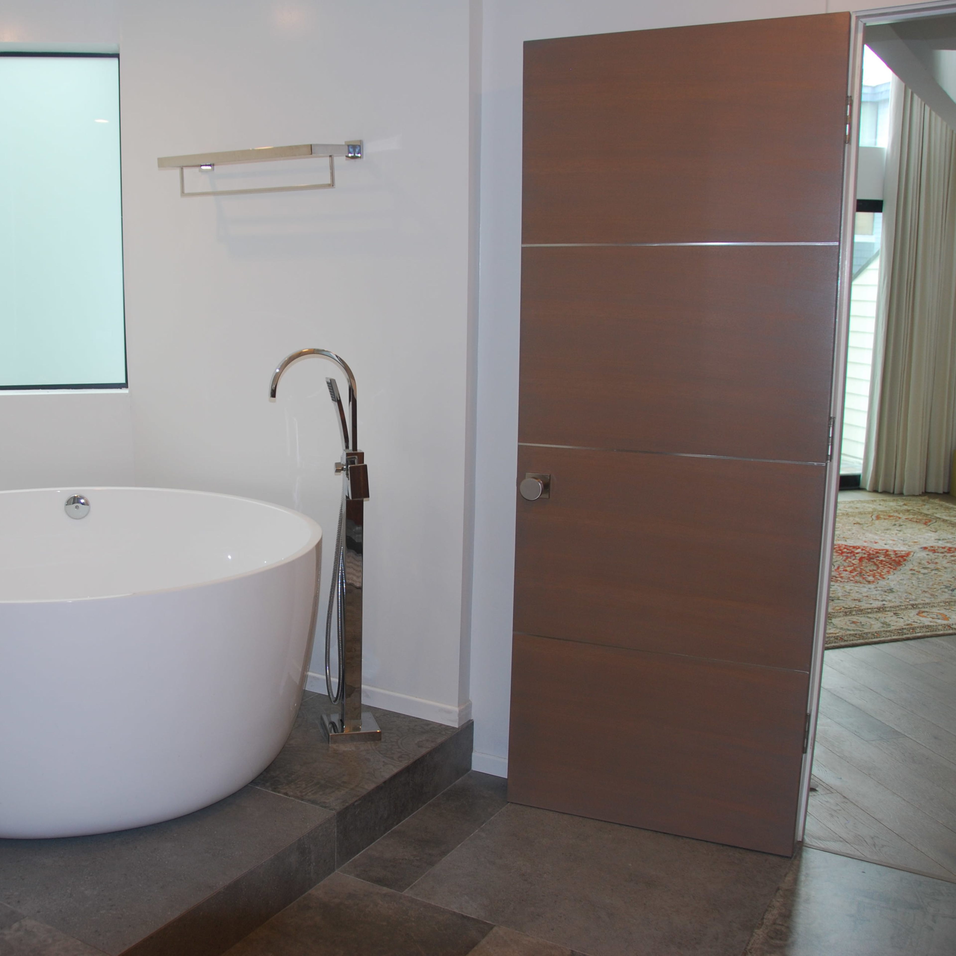 A modern bathroom featuring a round white bathtub next to a wooden door and a window.