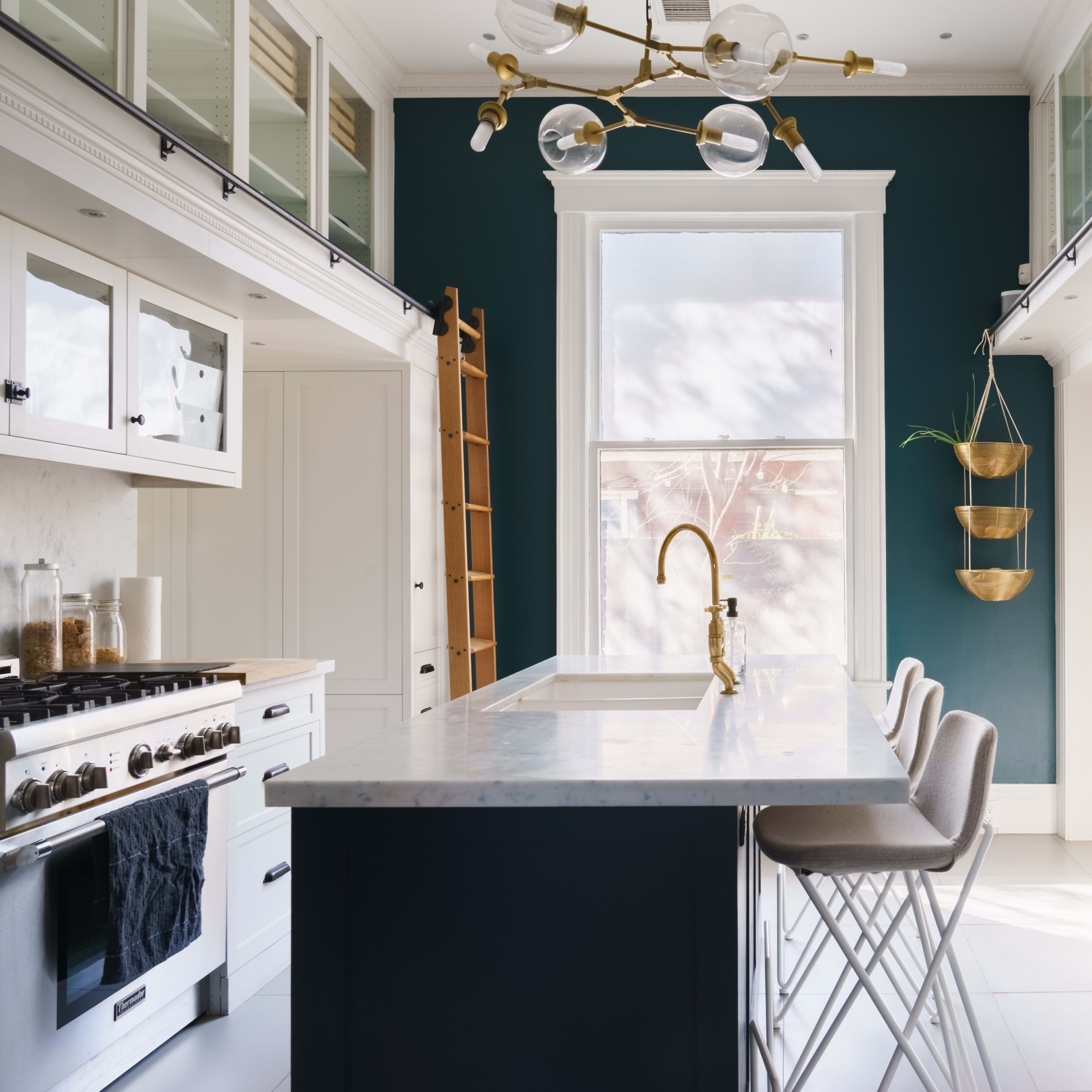 A modern kitchen with a dark green wall, marble countertops, and a three-seat bar area.